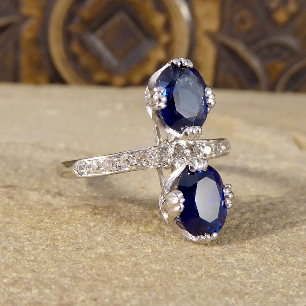 This beautiful Art Deco ring has been crafted in Platinum. Featuring a Diamond row along the band and two offset central Sapphires, above and below the band, this gorgeous ring could be a perfect engagement ring for any jewellery lover with a
