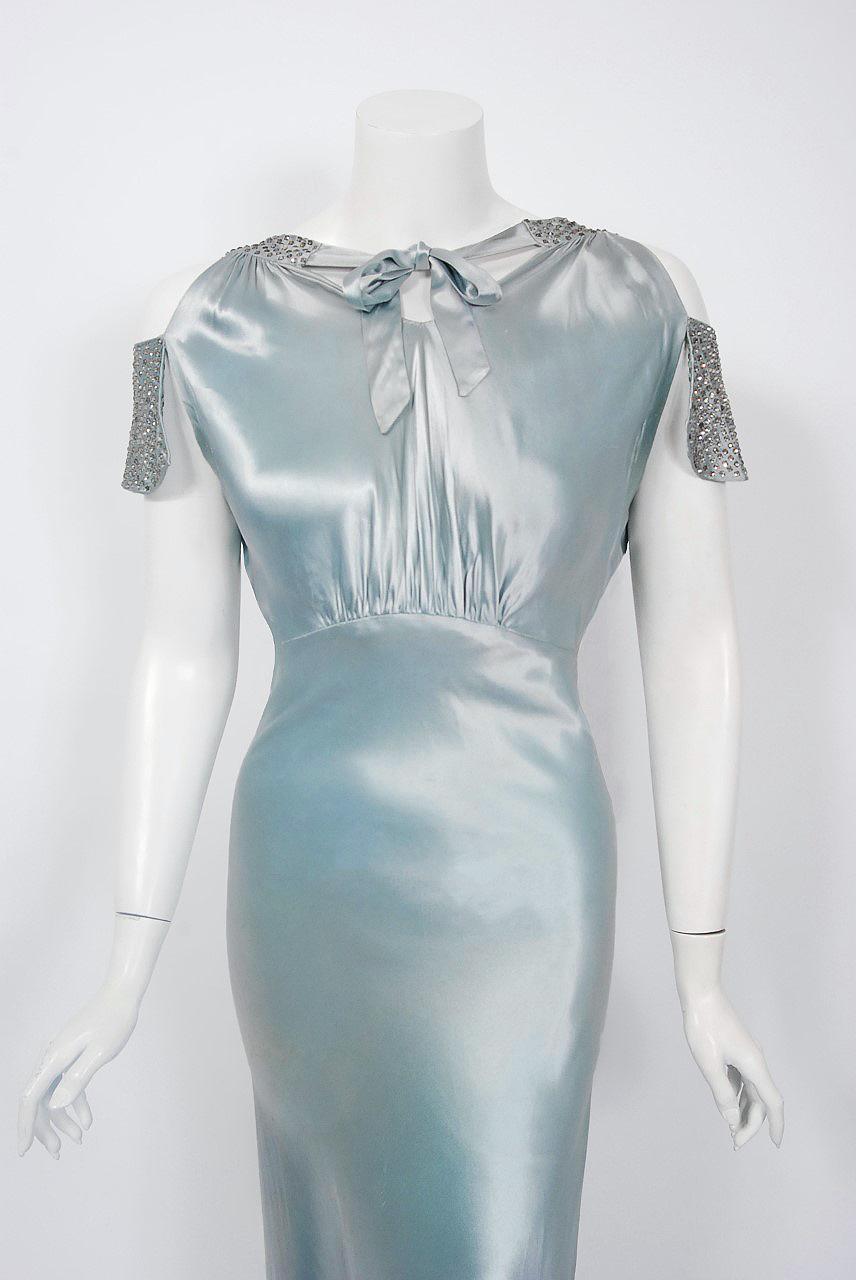 A breathtaking 1930's custom-made ice blue silk gown from the Old Hollywood era of glamour. There is so much detail, you can tell this masterpiece was created with love and care. The bodice has a sculpted bow-tie neck with flirty cut-out shoulders.