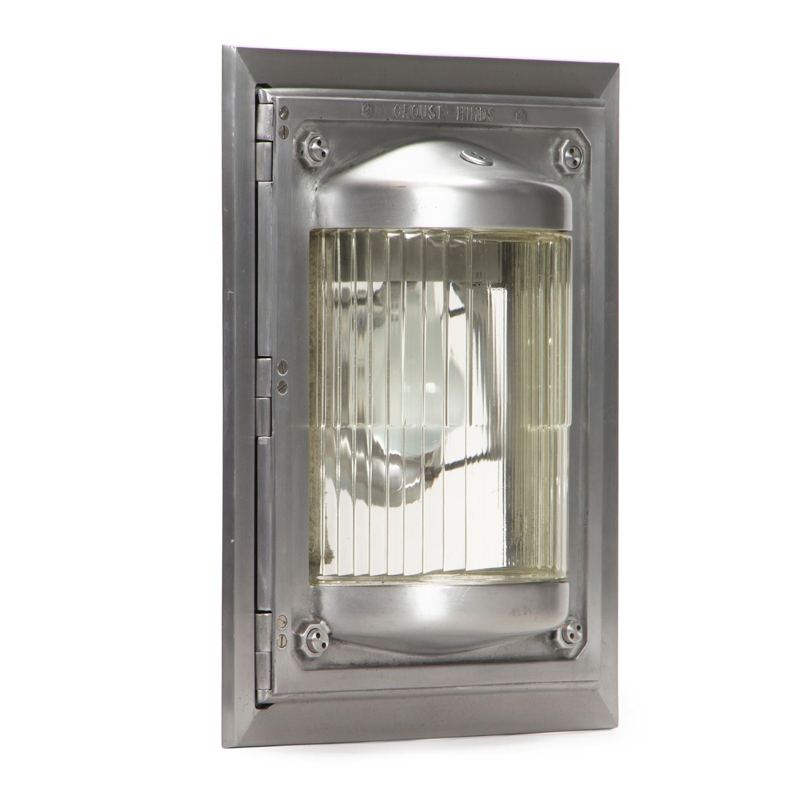 A large-scale, flush mount aluminum wall light with a ribbed cast glass shade, bearing the manufacturer's name. Similar to lights installed on the Hoover Dam.