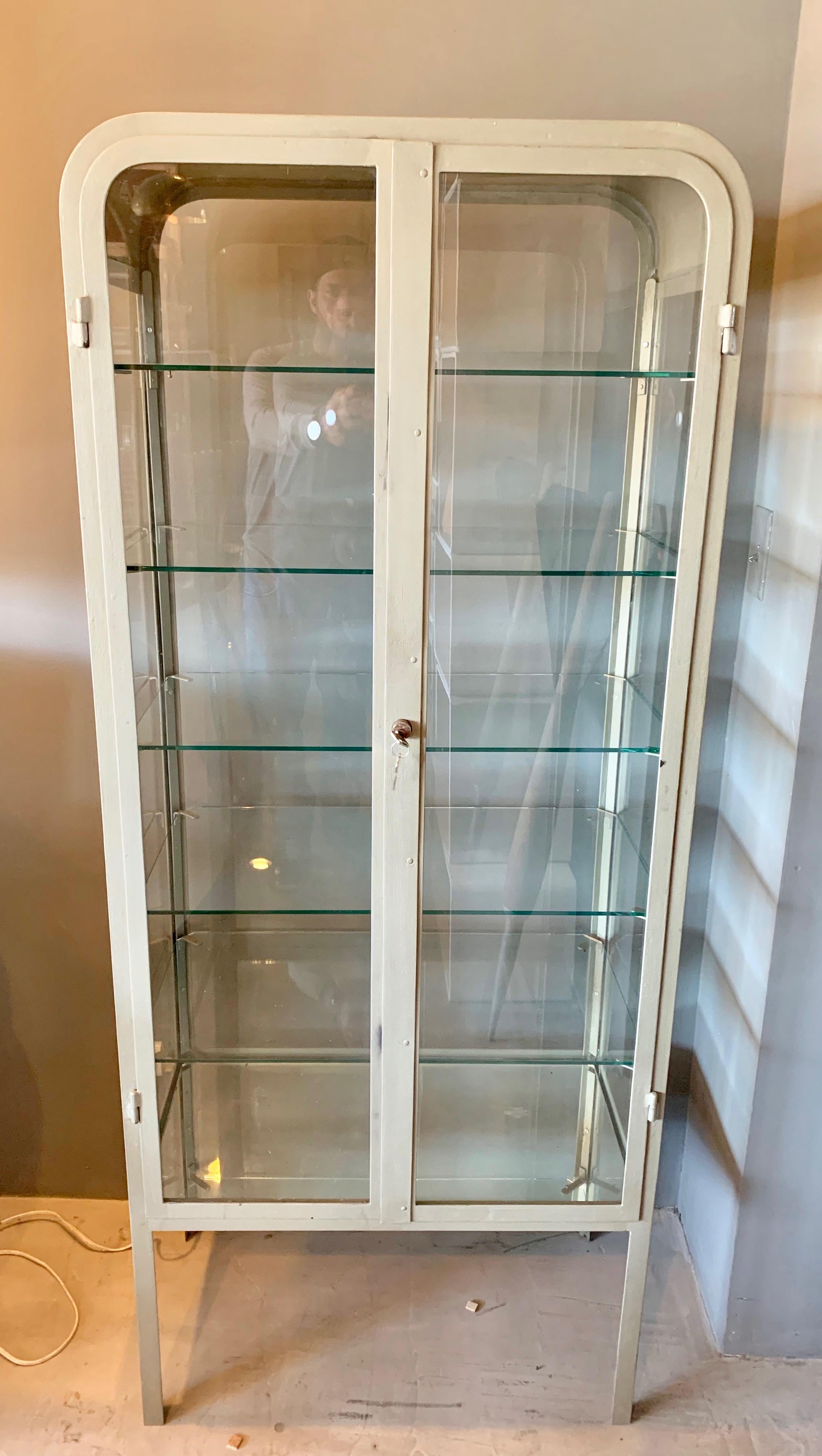 Handsome two-door iron and glass vitrine from Buenos Aires, circa 1930. Great vintage condition. Original working lock with 5 tempered glass shelves and antique mirror bottom. Back of display is also clear glass. Awesome display cabinet. 