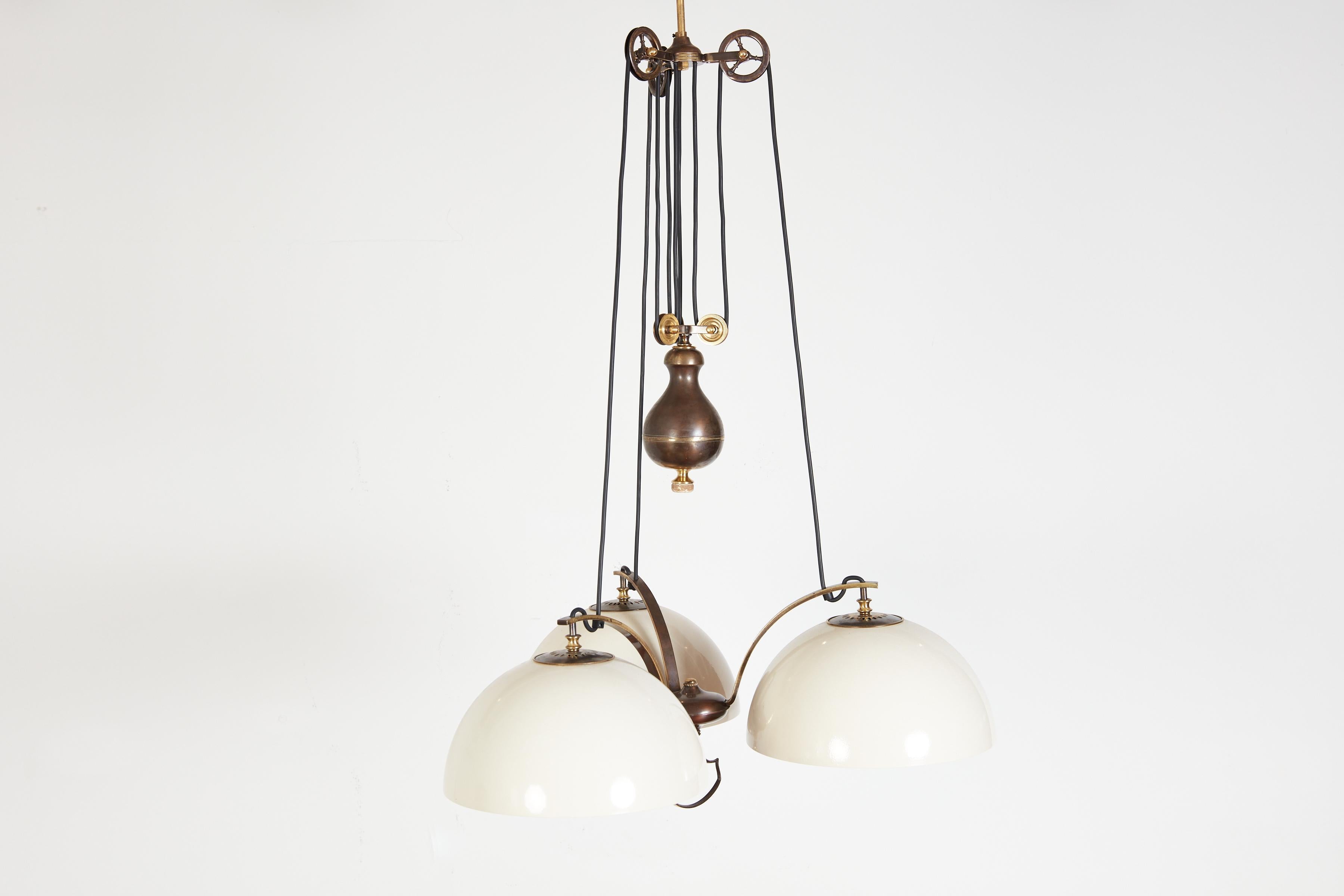 Wonderful counterbalance pendant with 3 creamy white dome shades and solid brass counterweight enabling the light to maneuver up and down.
Industrial brass wheel hardware with ornate curved brackets. 
Unique piece 
Italy, circa 1930s