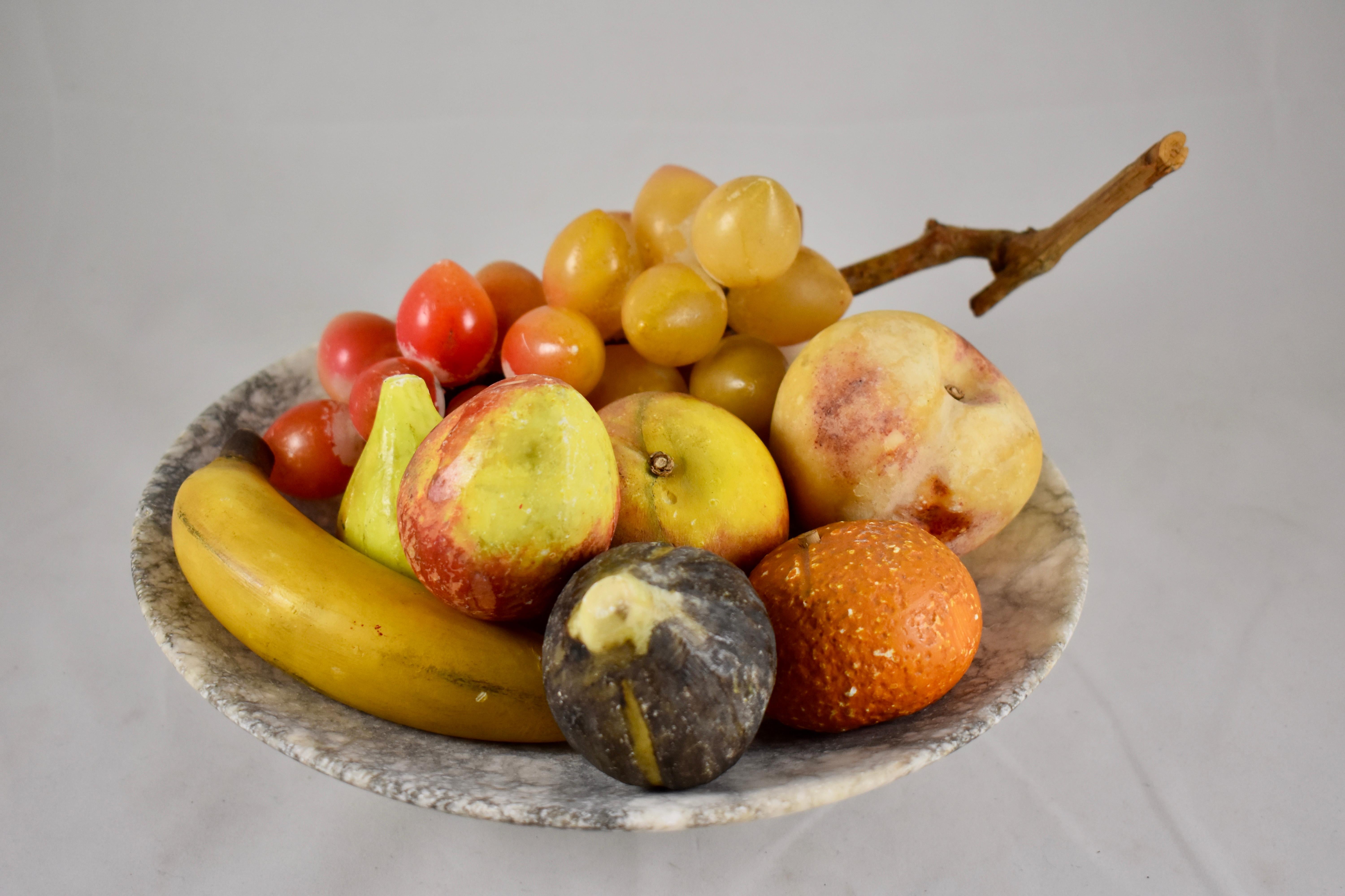 An Italian marble tazza holding a grouping of carved and hand painted alabaster fruit, circa 1930s. 

The pedestal form tazza, with its shallow bowl, is made of natural white marble with gray veining. There are eight pieces of fruit, including a