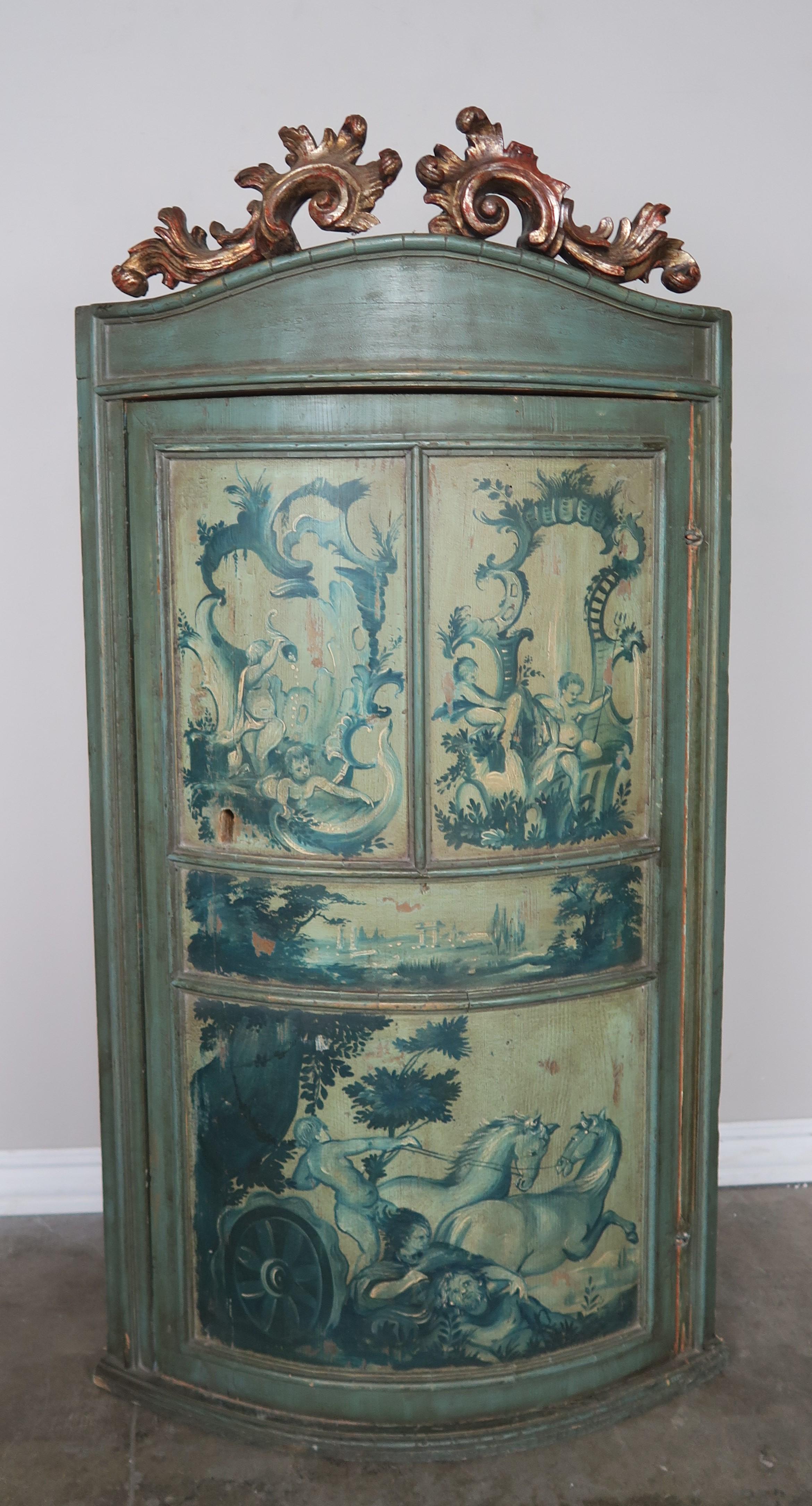 1930s Italian painted and parcel gilt corner cabinet. The piece is finely painted with cherubs and mythological scenes in soft shades of green and aqua blue. The top is also finely carved and finished in 22-karat gold leaf. Original working key