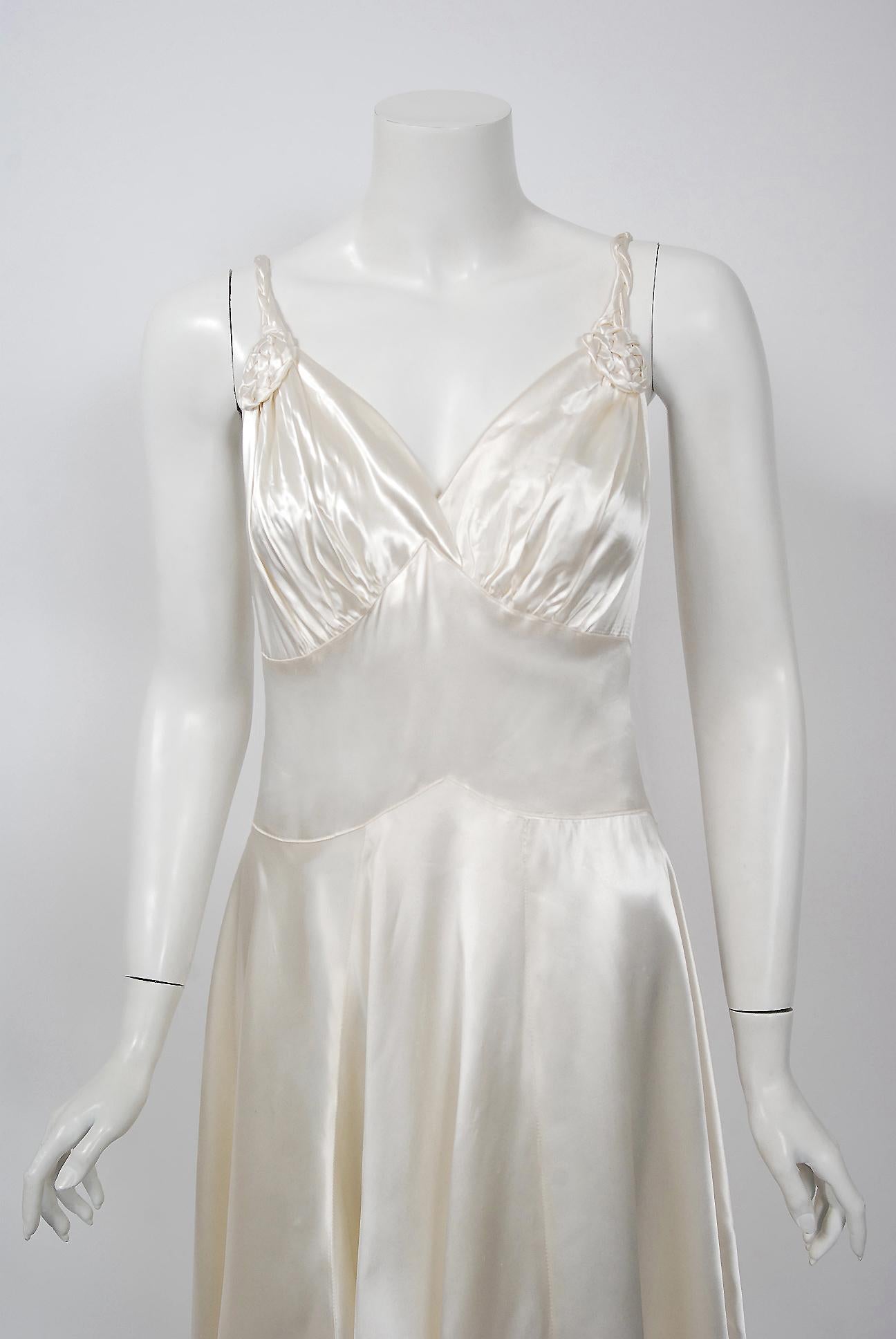An elegant 1930's custom made ivory silk-satin slip dress from the Old Hollywood era of glamour. The bodice has a seductive low-cut sculpted plunge with detailed rosette appliques. The thin braided straps and back covered buttons add the perfect
