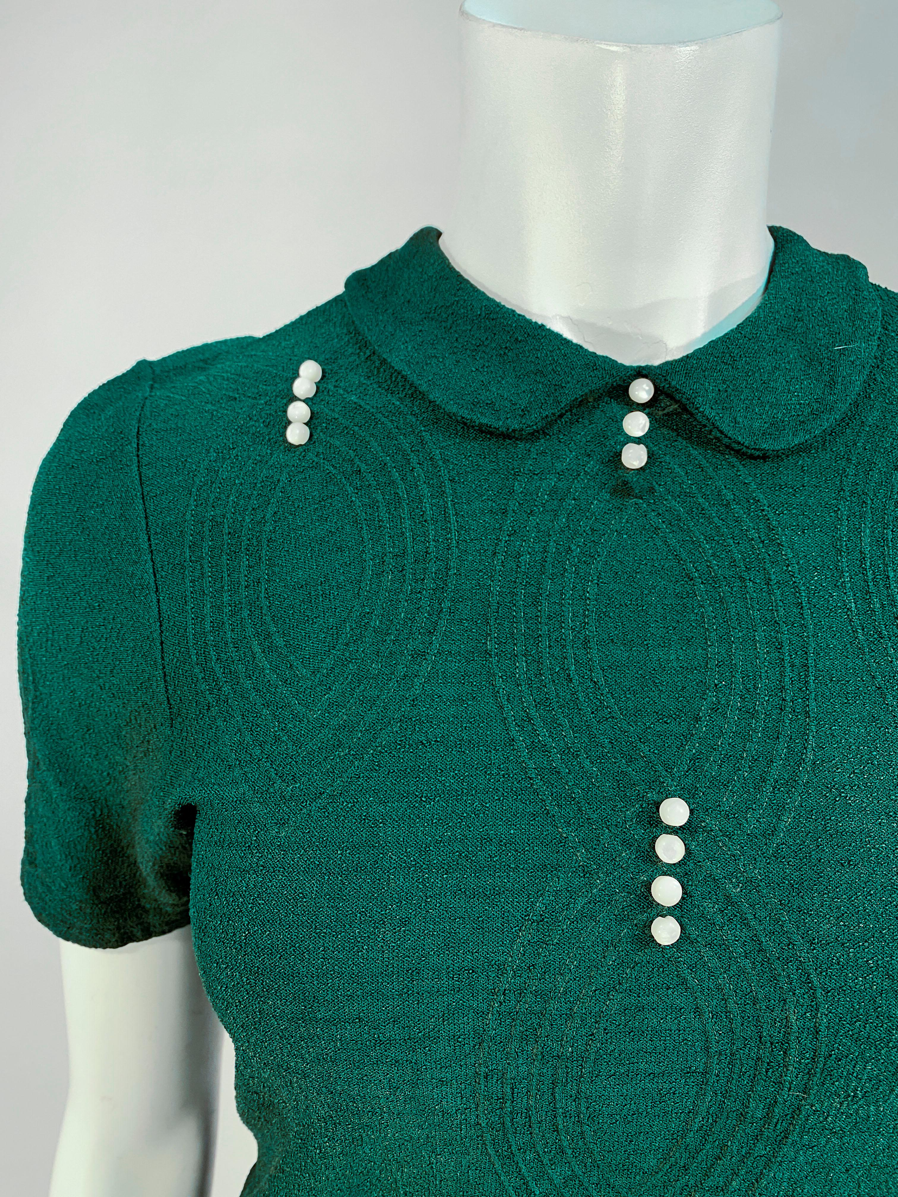 1940s Jack Frost forest green knit blouse with Art Deco patter accented with mother of pearl shell buttons, a petter pan collar, short sleeves, and flattering darts on was it and bust. 7-inch metal zip closure on the back of the neck.