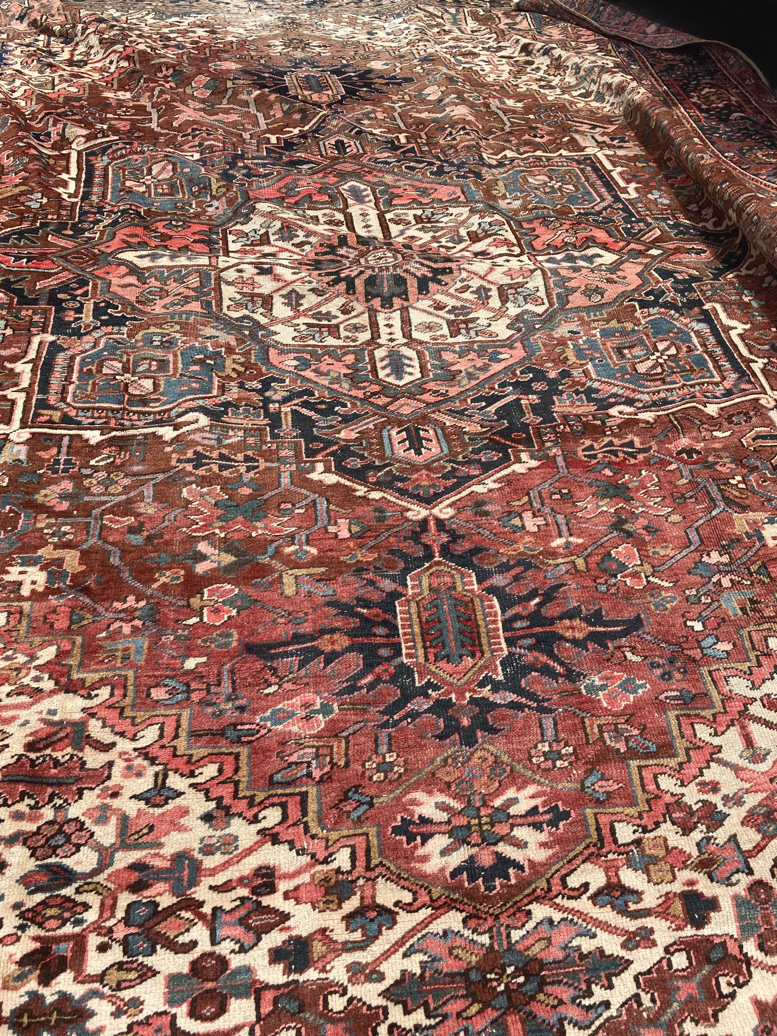 1930s Heriz rug with a rich palette of red, blue, and ivory hues. A large central medallion sits on a dark red field is surrounded by an ornate patterning of tree and vine motifs. This pattern repeats throughout, creating a lush composition.