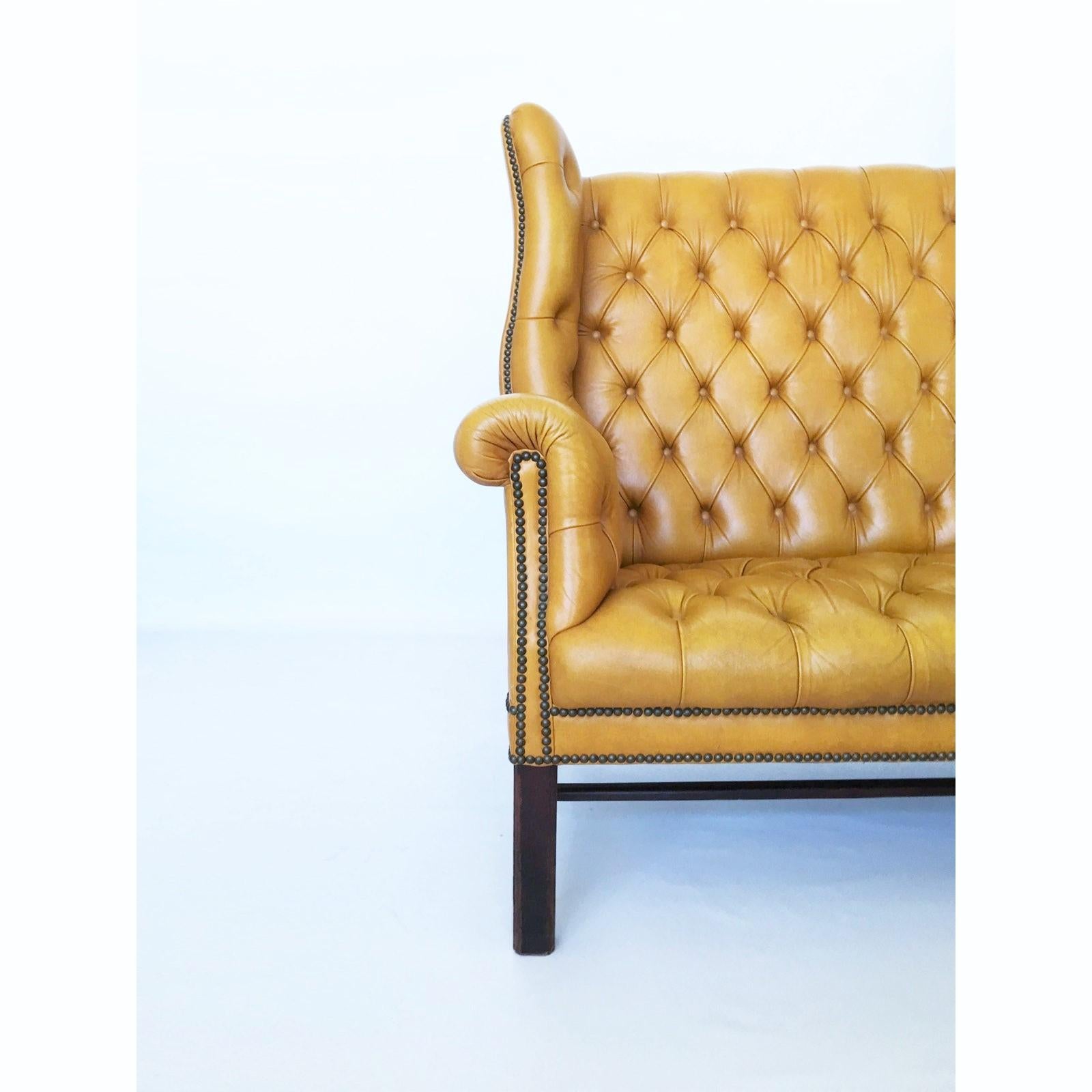 This handsome George III style wing back tufted leather settee is the definition of old fashioned luxury. Featuring a warm mustard leather tufting with out-scrolled wings & arms all resting on square Marlboro front legs & splayed back legs that are