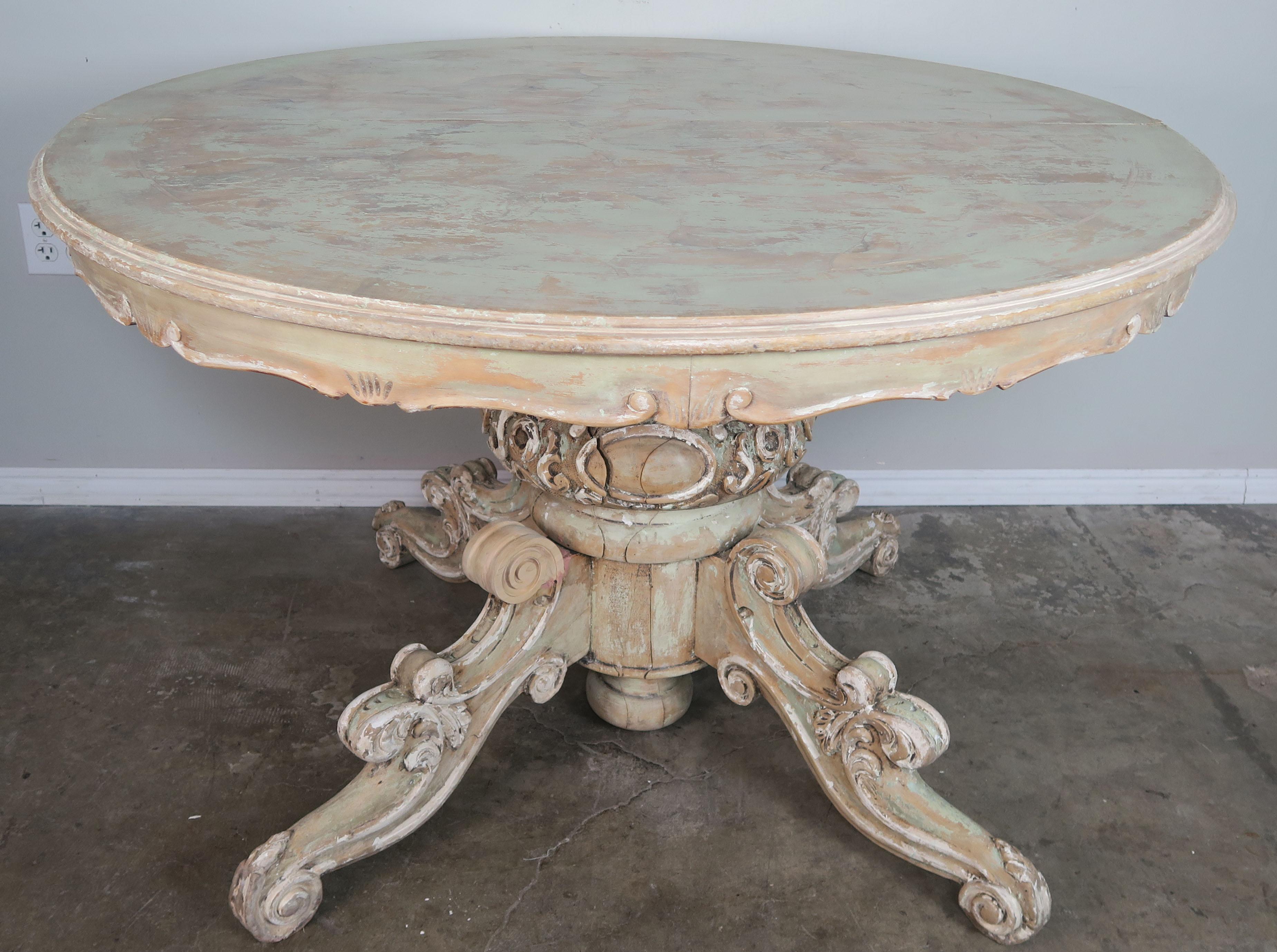 1930s French carved wood Louis XV pedestal dining table. Beautiful distressed finish with remnants of paint throughout. Scalloped apron and beautifully carved center that extends into four carved scrolled legs. Perfect for a small dining room or