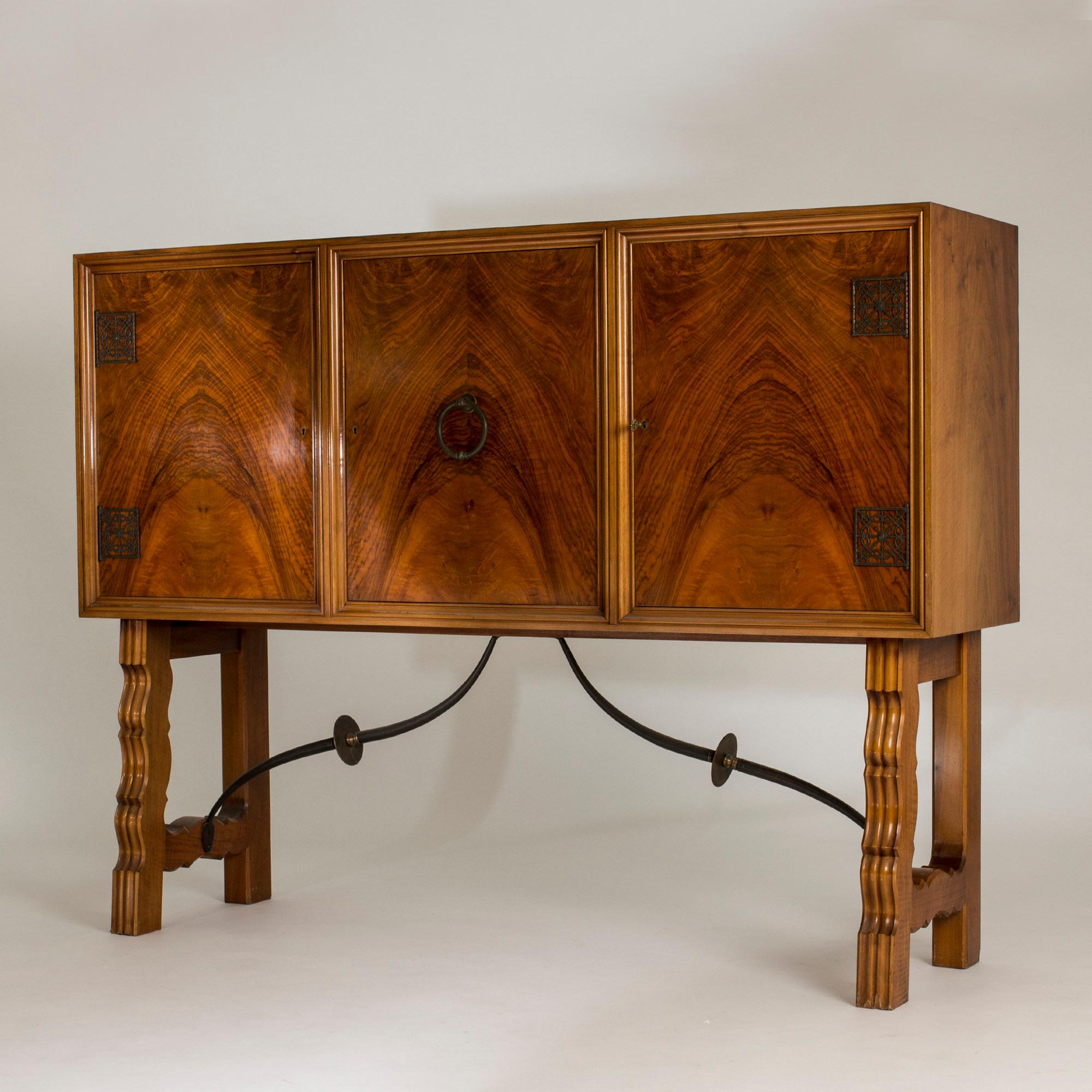 Striking, tall mahogany cabinet by Otto Schulz with dramatic veneer on the front. Baroque inspired design details with robust sculpted legs, brass decorations in the corners and a knocker in the center. Beautiful flowing metal extenders under the