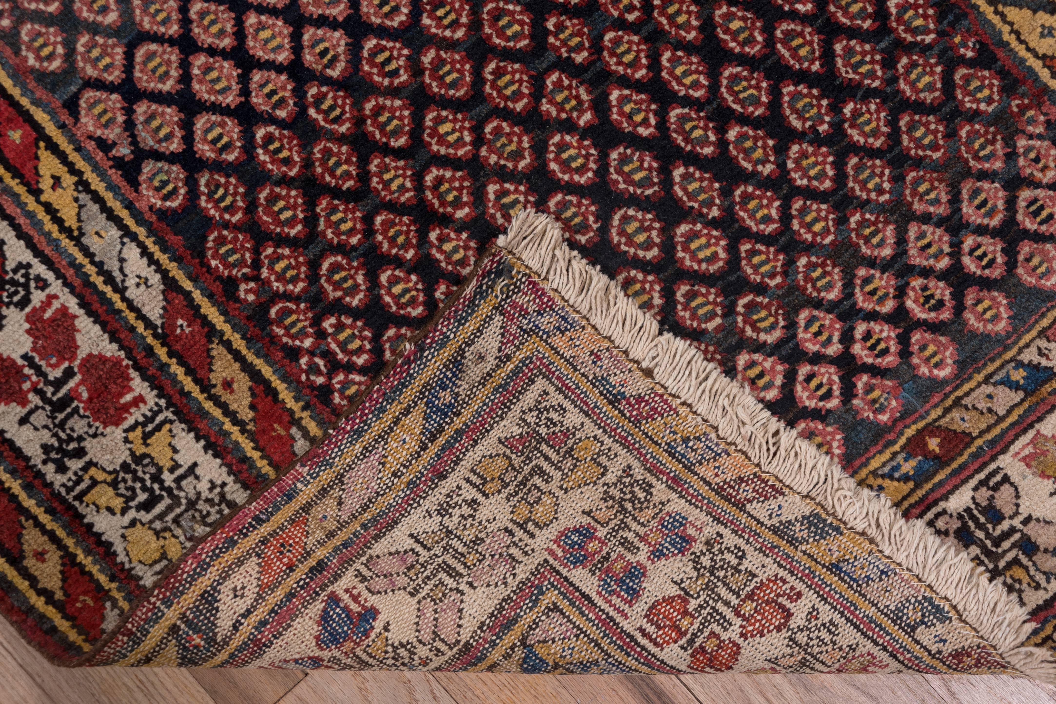 This Western Persian village runner has an abrashed dark brown field with an all-over pattern of small multi colored semi-octagons. The ivory main border displays colorful triple flower motifs. The minor borders are both in a broad barber full style