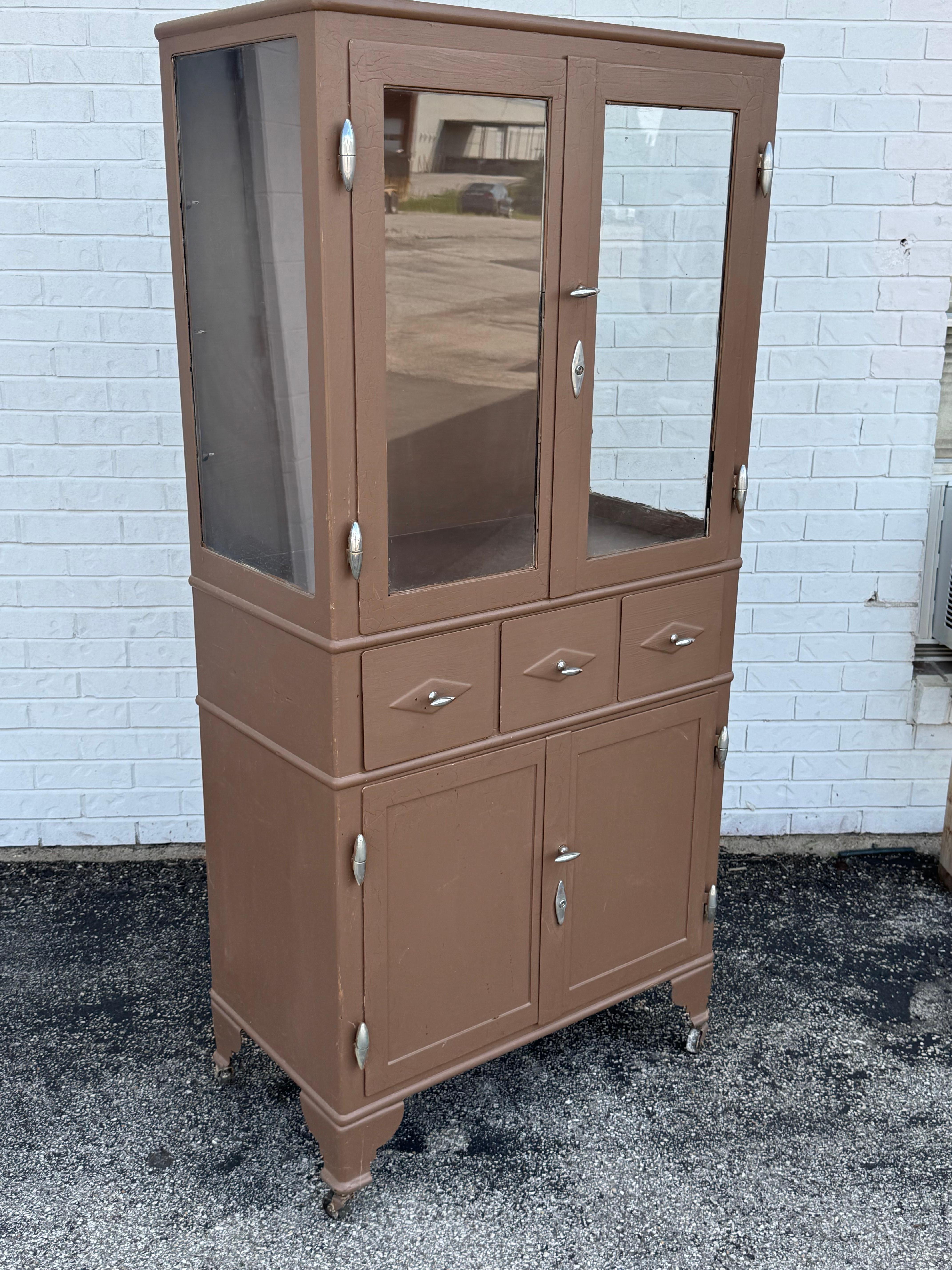 Autentico armadietto medico industriale in metallo vintage degli anni '30 per esporre e conservare i tuoi oggetti da collezione su rotelle. Le porte anteriori a doppio vetro si aprono su scaffali regolabili; si noti che i ripiani in vetro originali