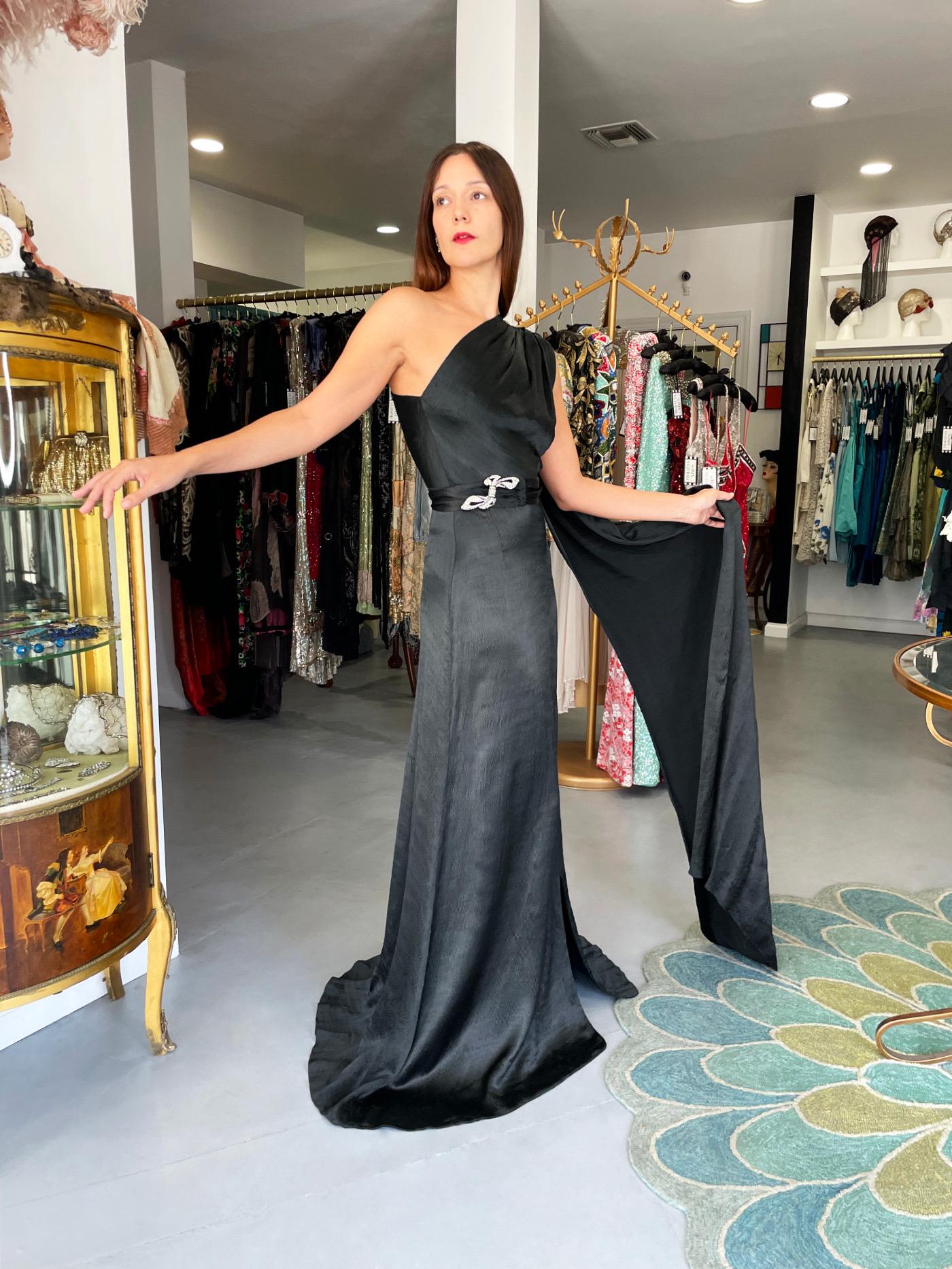 This incredibly chic and ultra rare Sally Milgrim couture black silk draped asymmetric one-shoulder trained gown dates back to the mid 1930's. Sally Milgrim, a successful and influential businesswoman who preceded her American and European
