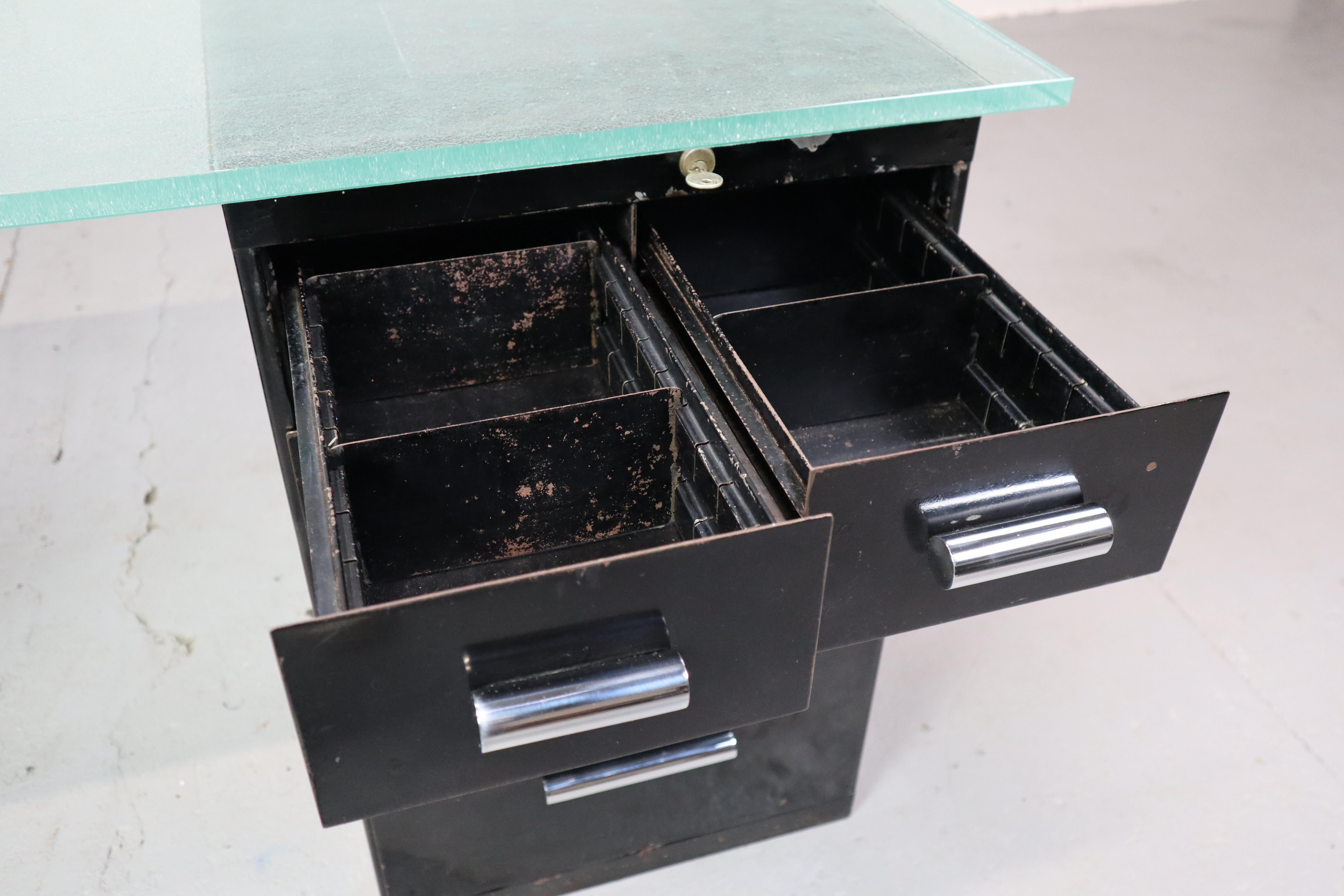 Scrivania modernista degli anni '30 in metallo laccato nero, maniglie nichelate e sormontata da una spessa lastra di vetro di Saint Gobain. Con serratura funzionante sui cassetti!
Nello stile di Bruno Weil per Thonet.
Dxhxl: 72x76x167 cm

Questa
