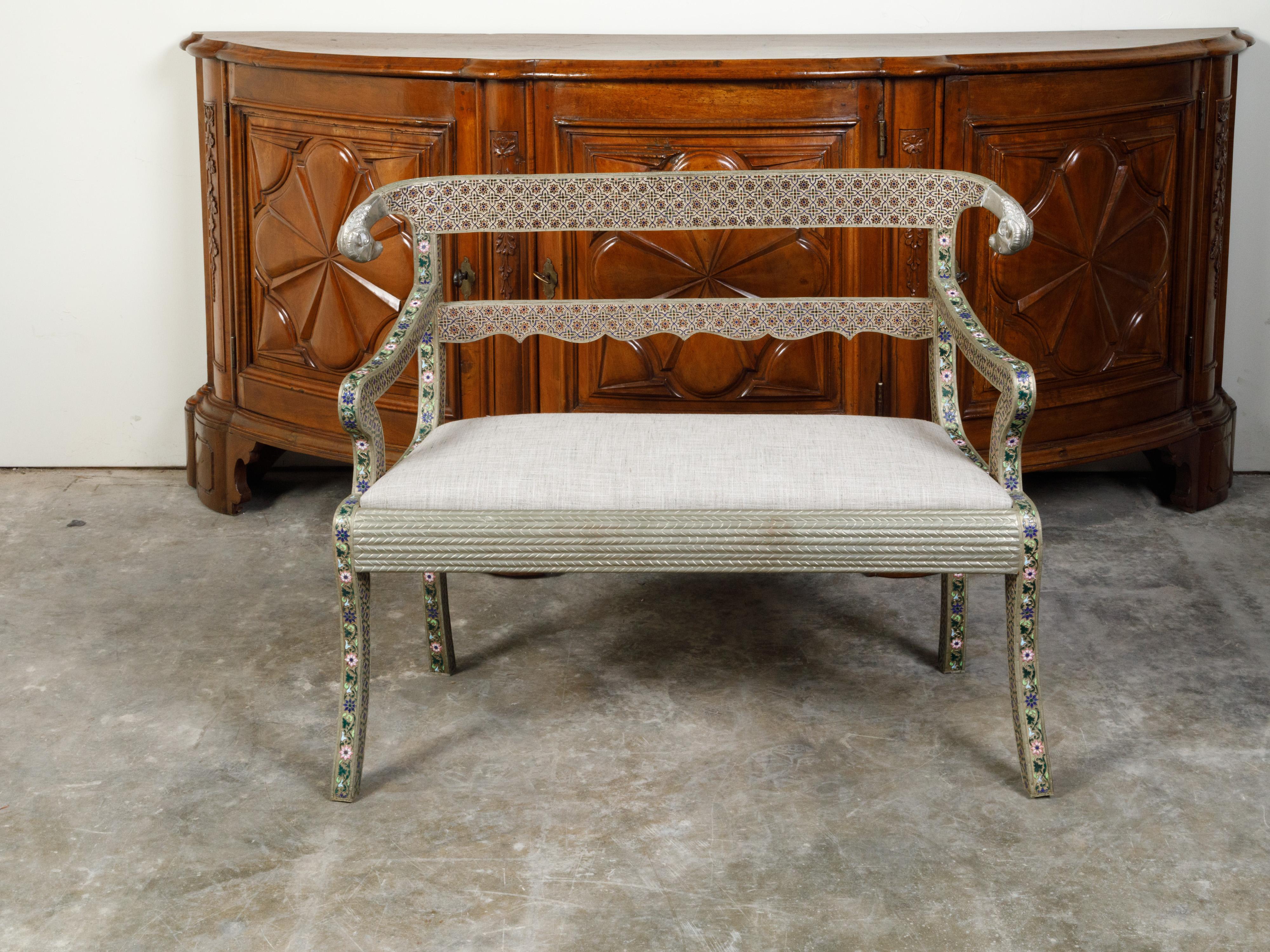 A Moroccan metal settee from the mid 20th century, with enamel décor and rams' heads. Created in Morocco during the second quarter of the 20th century, this settee features a pierced back accented with rams' heads and scalloped splat, connected to
