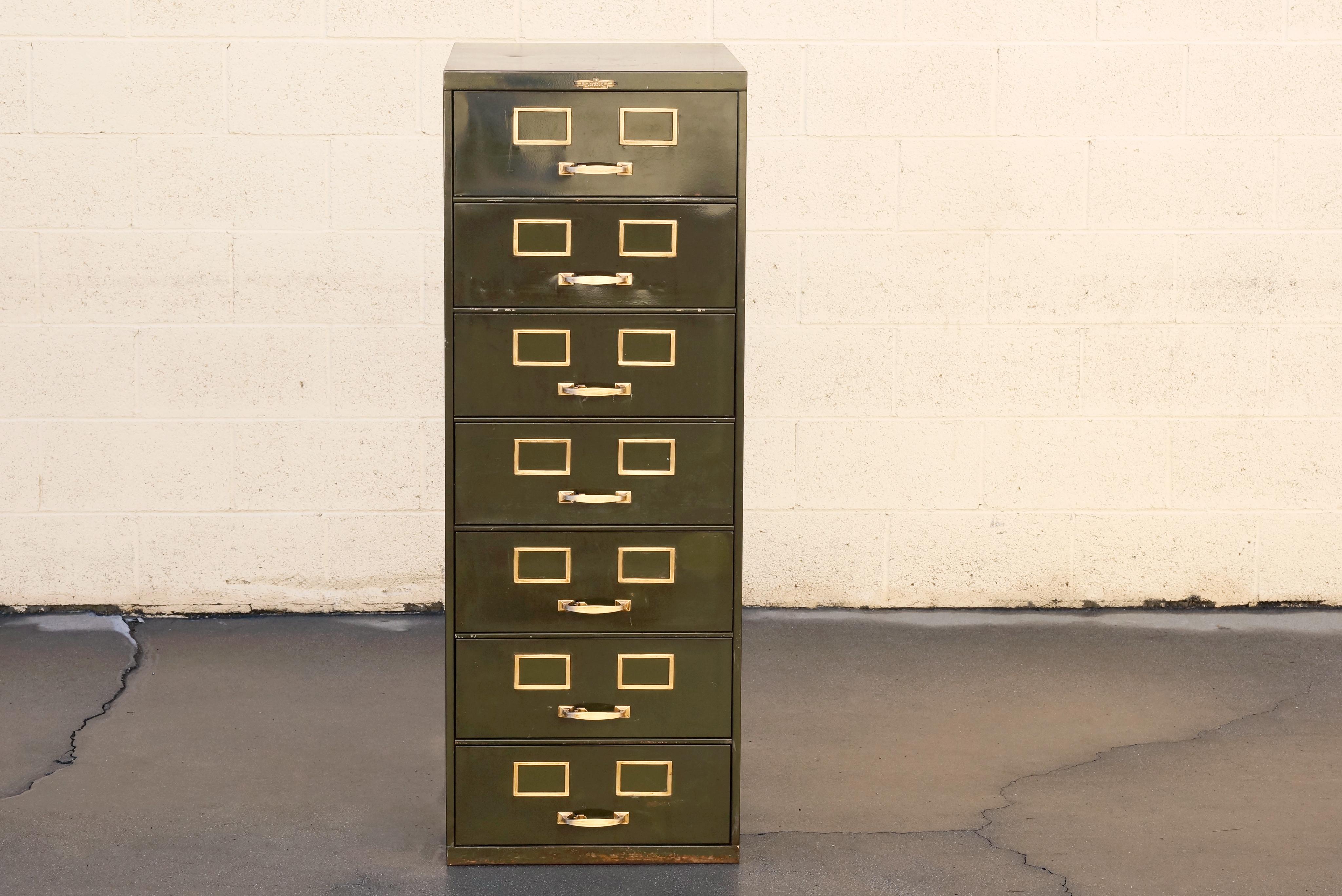 Classic American multi drawer card filing cabinet by Remington Rand. Industrial era, composed of steel. Original army green paint with characteristic patina. Original polished brass hardware and label. Features seven drawers, circa