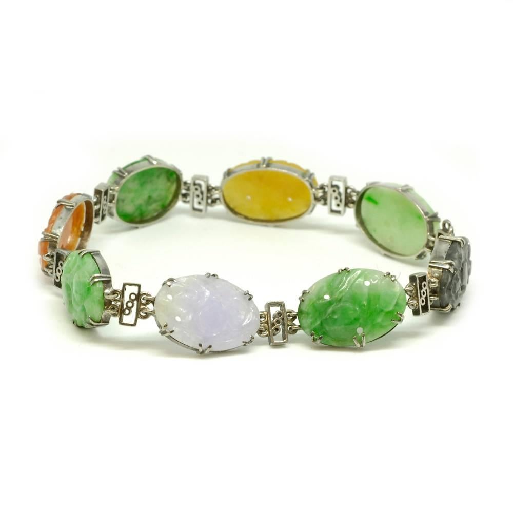 A jade panel bracelet. The oval jade panels in shades of green, lilac, reddish-orange, yellow and black, each pierced and carved with foliate decoration, spaced by openwork, rectangular links, mounted in 9ct white gold.  English circa 1930.