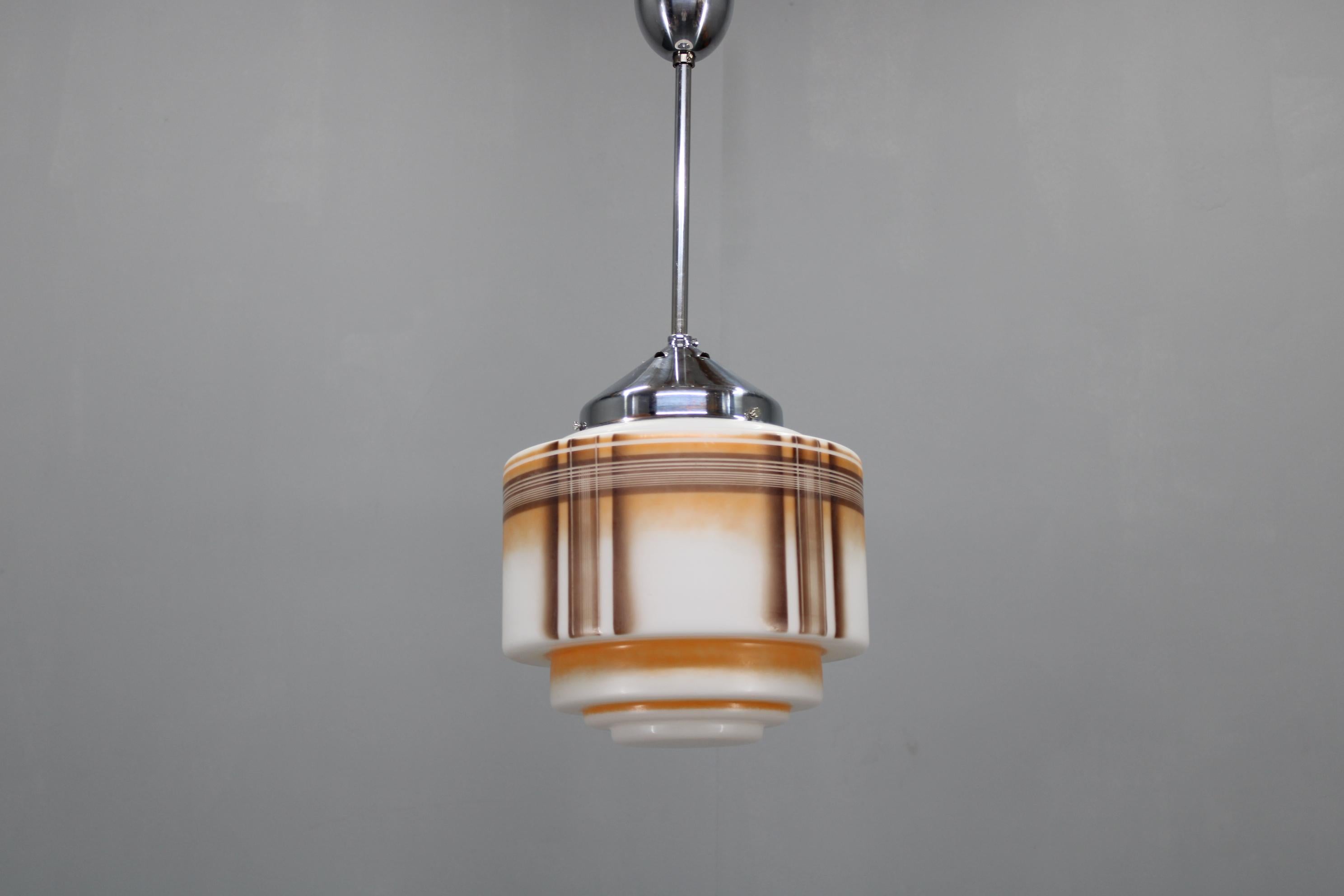  This exquisite 1930s Art Deco pendant light by NAPAKO showcases the refined geometry and functional elegance of Czechoslovak modernist design. The chromed metal holder pairs with a richly patterned glass shade featuring stepped forms and warm