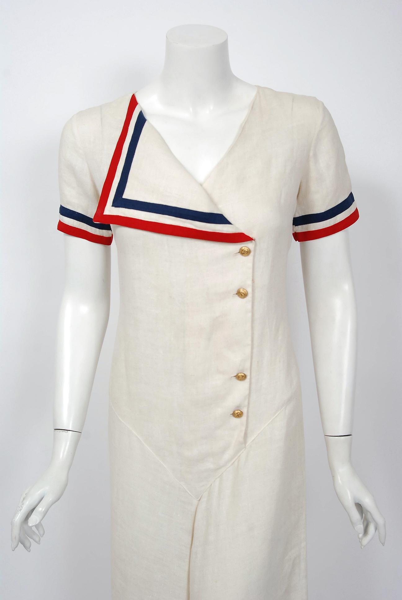 A breathtaking and rare nautical sailor ivory linen jumpsuit from the late 1930's Old Hollywood era of glamour. The bodice has a gorgeous off-center wide lapel with brass anchor motif buttons. I love the red and blue patriotic striped bands which