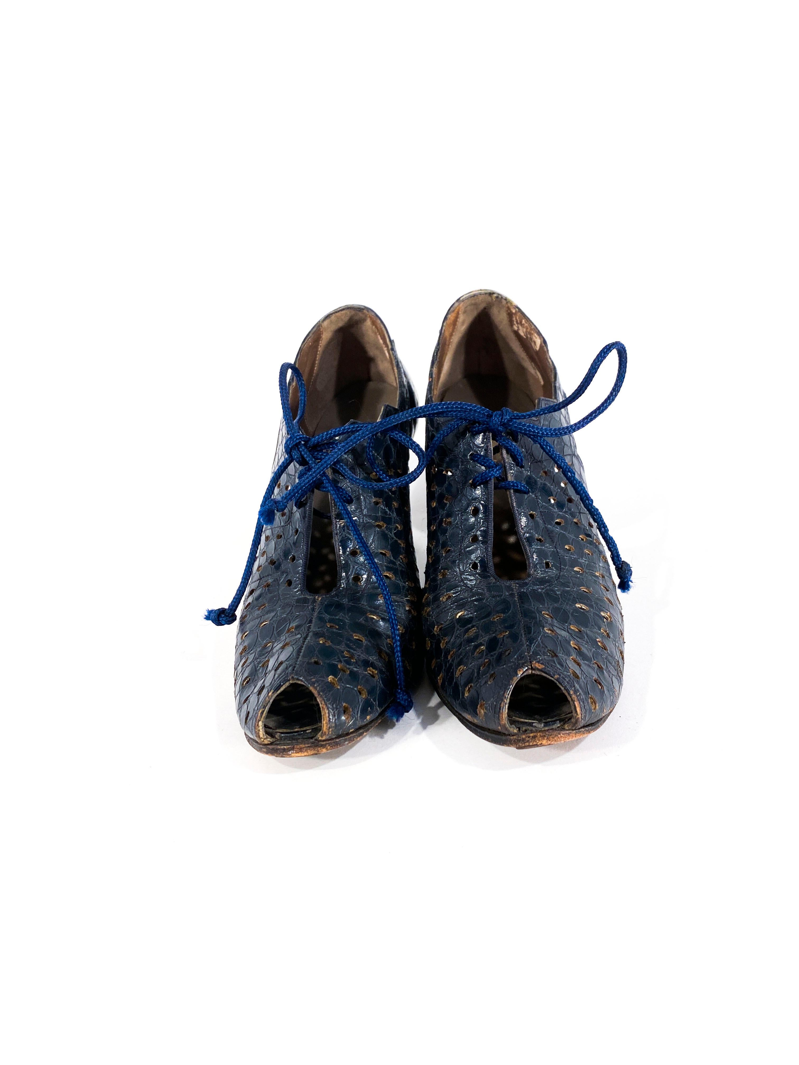chaussures à talon Art Déco des années 30 en alligator bleu marine avec de grandes découpes sur les côtés de la chaussure. Le corps des chaussures est orné de trous de perçage et d'un lacet. Les talons ont une hauteur de 10 cm et sont recouverts