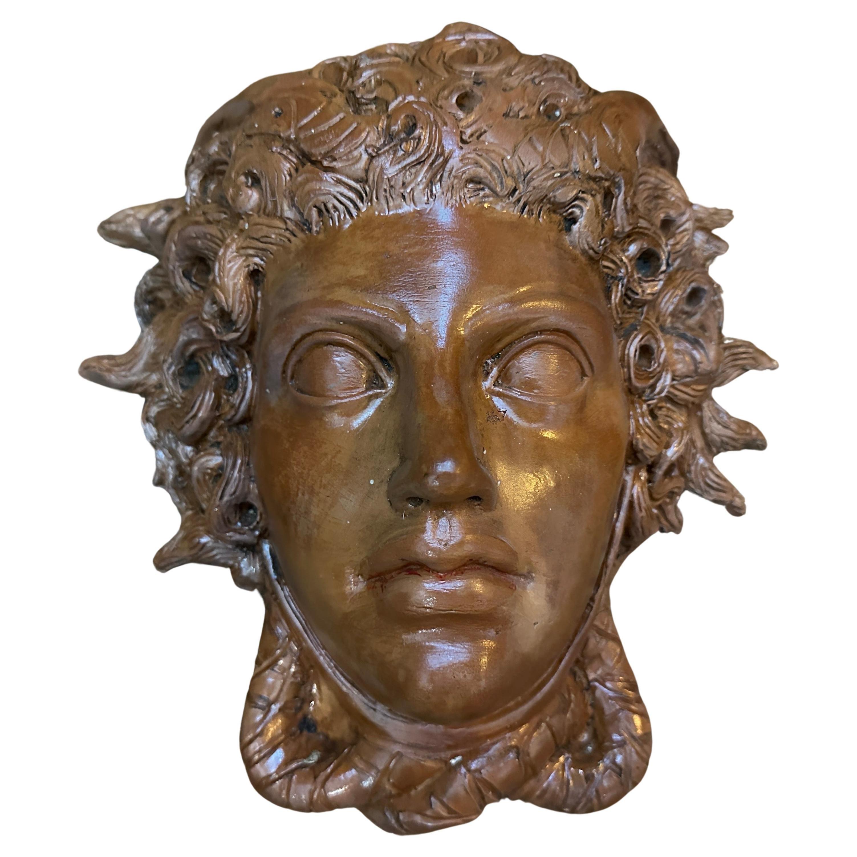 Una testa di Medusa in terracotta smaltata realizzata a mano a Caltagirone, piccola città della Sicilia famosa per le ceramiche artigianali. La testa ha uno smalto marrone con segni di età. Medusa, una figura della mitologia greca nota per i suoi
