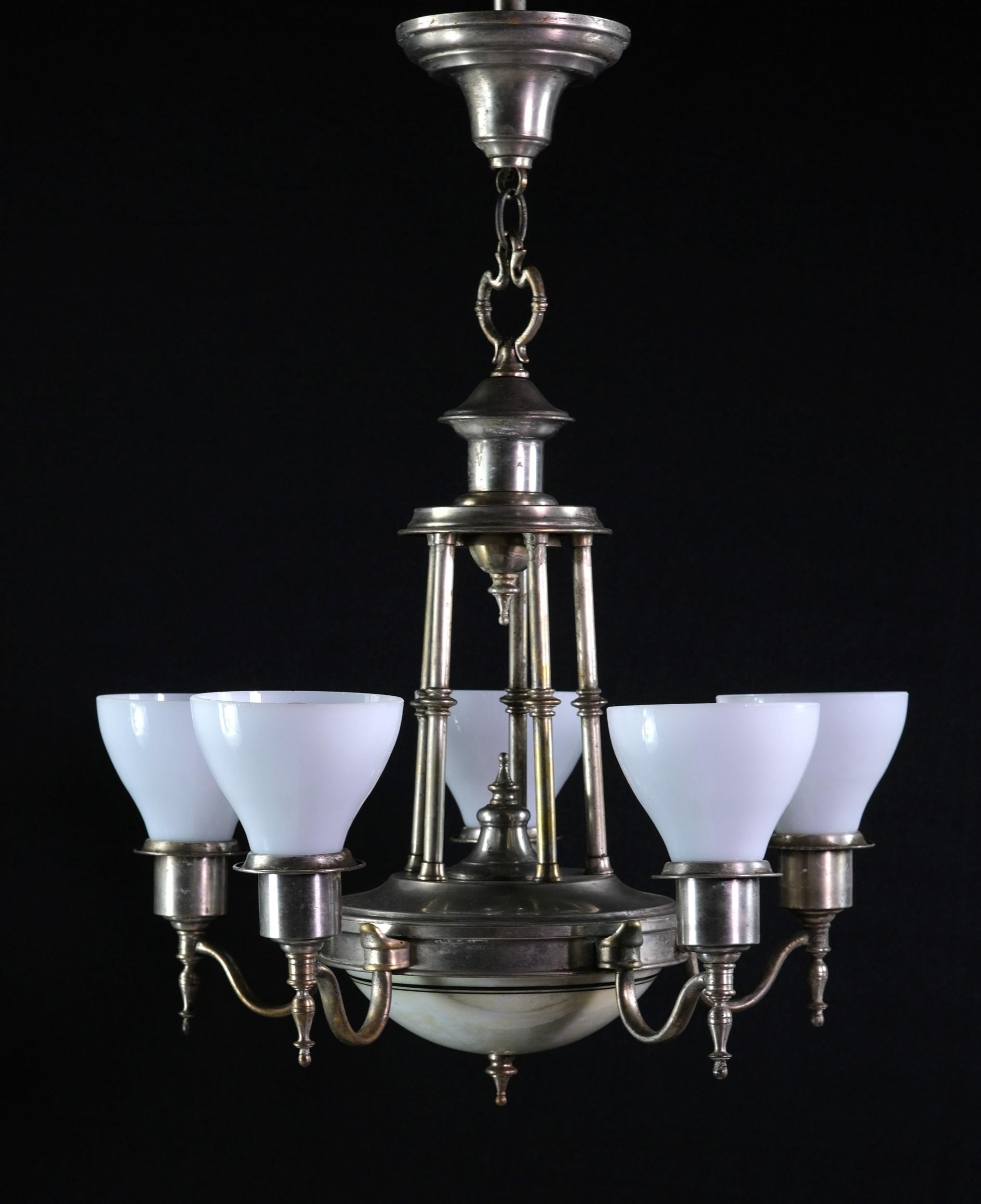 This classic 1930's five-arm chandelier is nickel-plated over brass with milk glass shades. 
The bottom features an additional light with a dish shade decorated with a green pinstripe. The accents include finials and decorative supporting rods. The