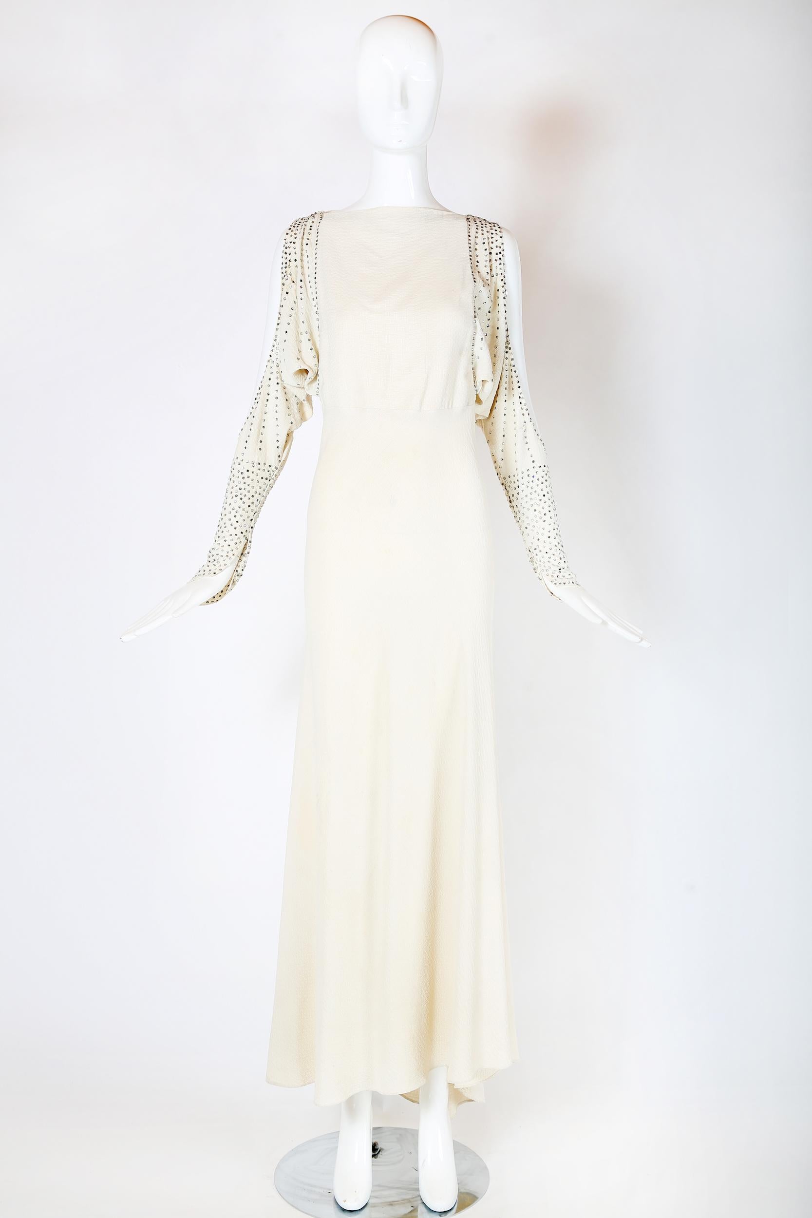 A 1930's bias cut puckered silk off-white goddess gown with cutouts at the back and sleeves. Studded with rhinestones at the sleeves and shoulder. In good vintage condition with some scattered invisible repairs, light marks, a tiny almost