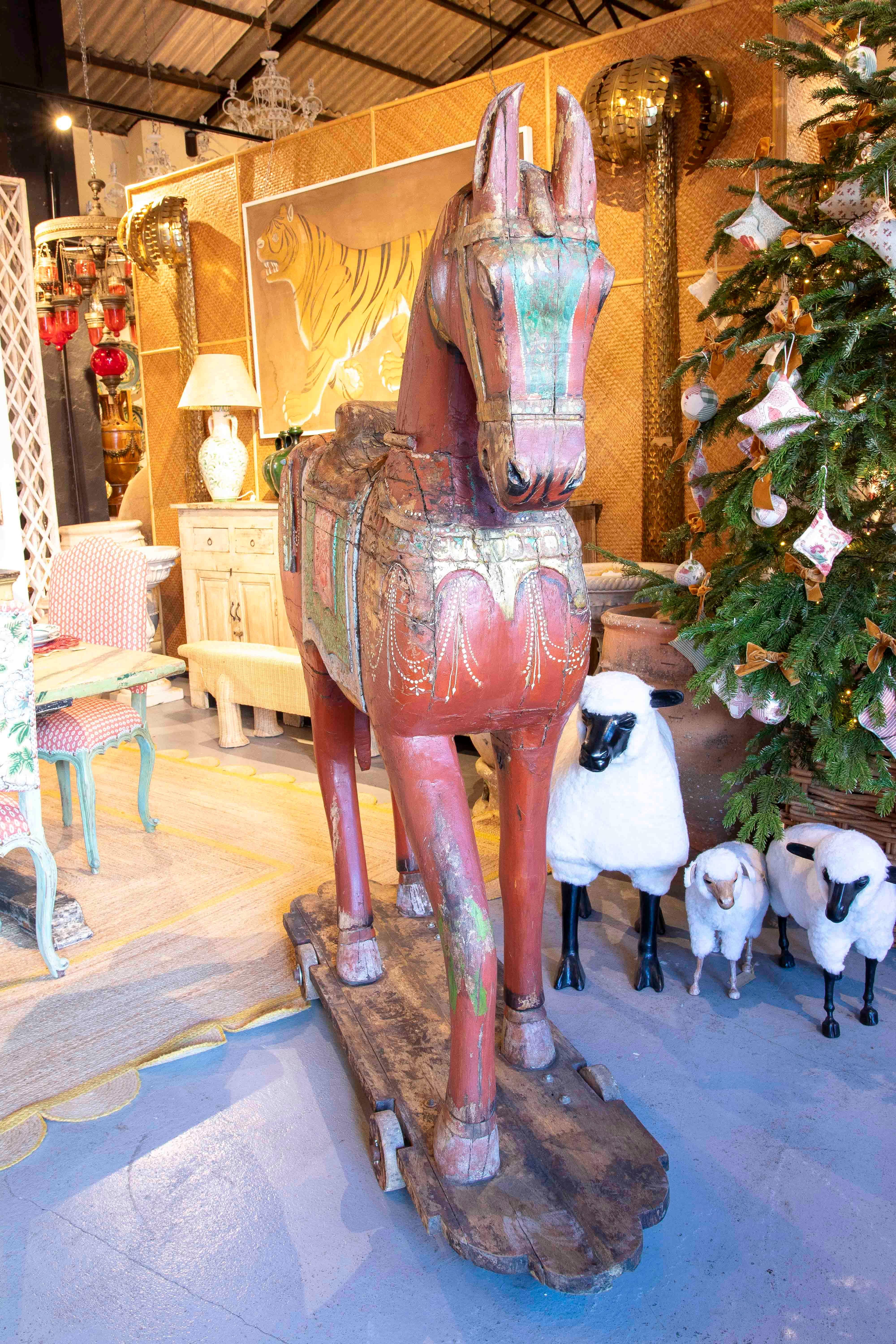 Beautiful pair of horses carved in wood, hand painted with vibrant colors such as red, green and golden details that evoke a classic and nostalgic style. Each horse is mounted on a wooden base with wheels, enhancing its authenticity and vintage