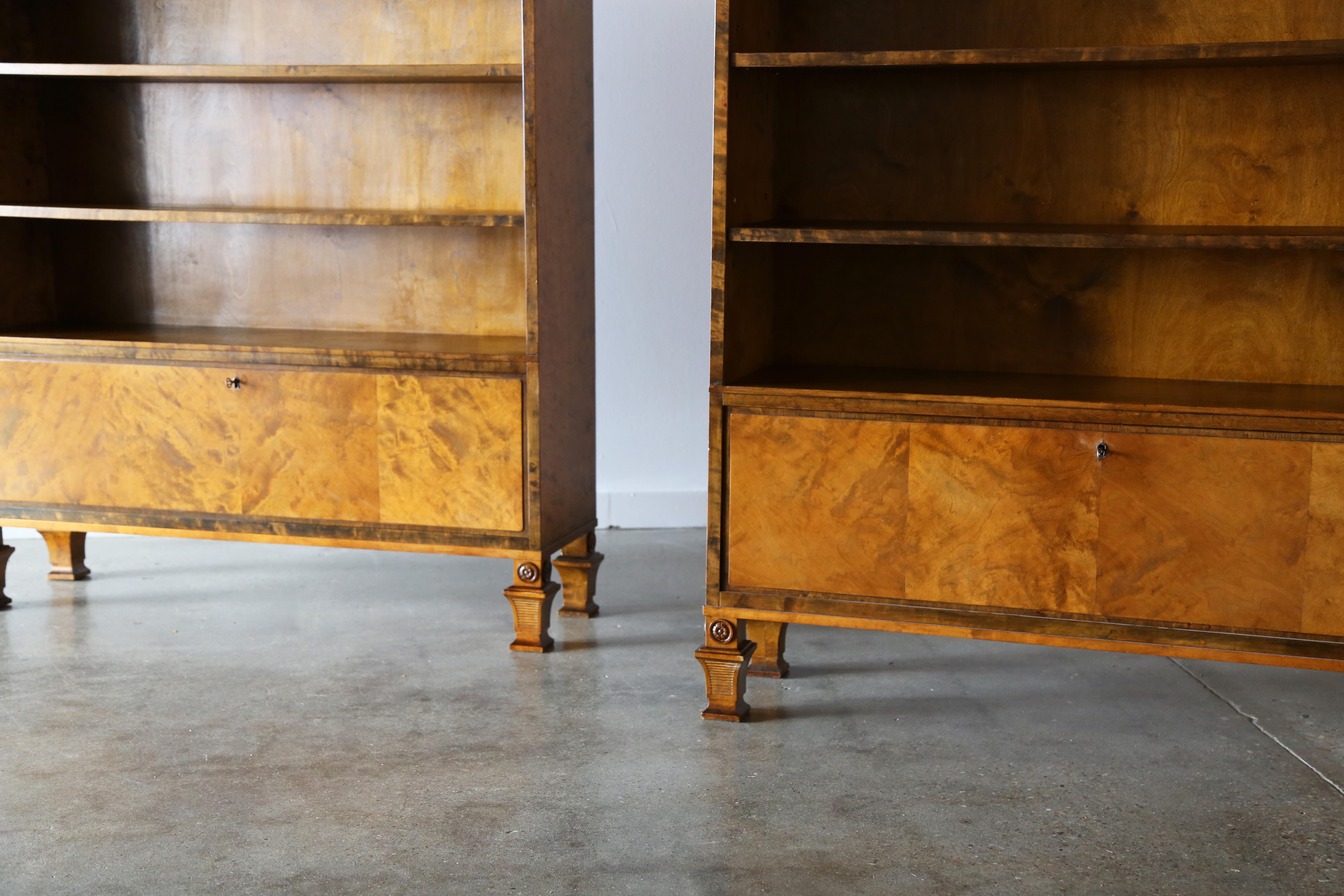 Una coppia di librerie o armadietti in stile Art Déco svedese di Carl Malmsten per SMF. La cassa è composta da legno di betulla a fiamma dorata altamente figurato con fasce e intarsi in palissandro. Piedi scolpiti in rilievo con medaglioni ornati. I