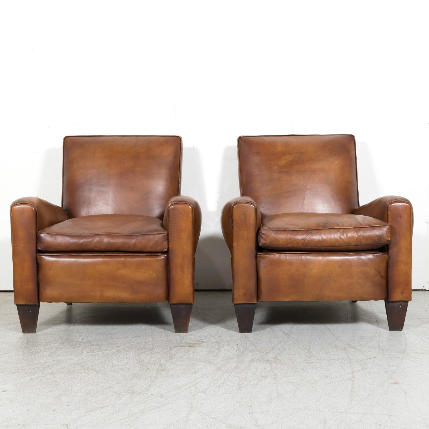 A handsome pair of French Art Deco period cognac leather club chairs, circa 1930s. Handcrafted in Paris, this classic pair of club chairs showcases superb craftsmanship and attention to detail, capturing the essence of Art Deco style with their