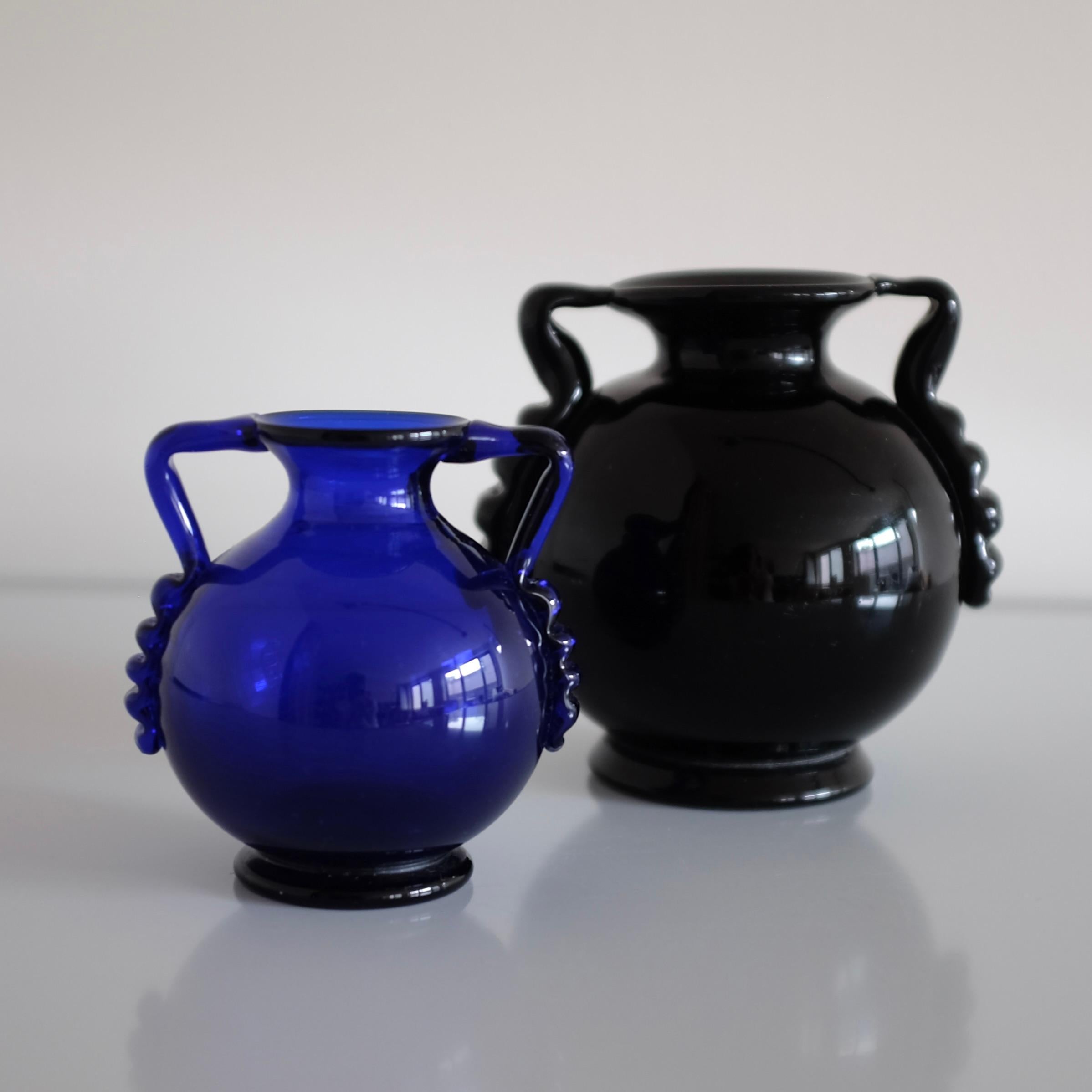 Coppia di vasi di vetro svedesi di metà secolo degli anni '30. Bellissimi dettagli ondulati sui manici con fondo rotondo, uno di colore nero e uno di colore blu. Usura appropriata all'età e buone condizioni vintage.

Dimensioni:

Vaso nero: H. H. x