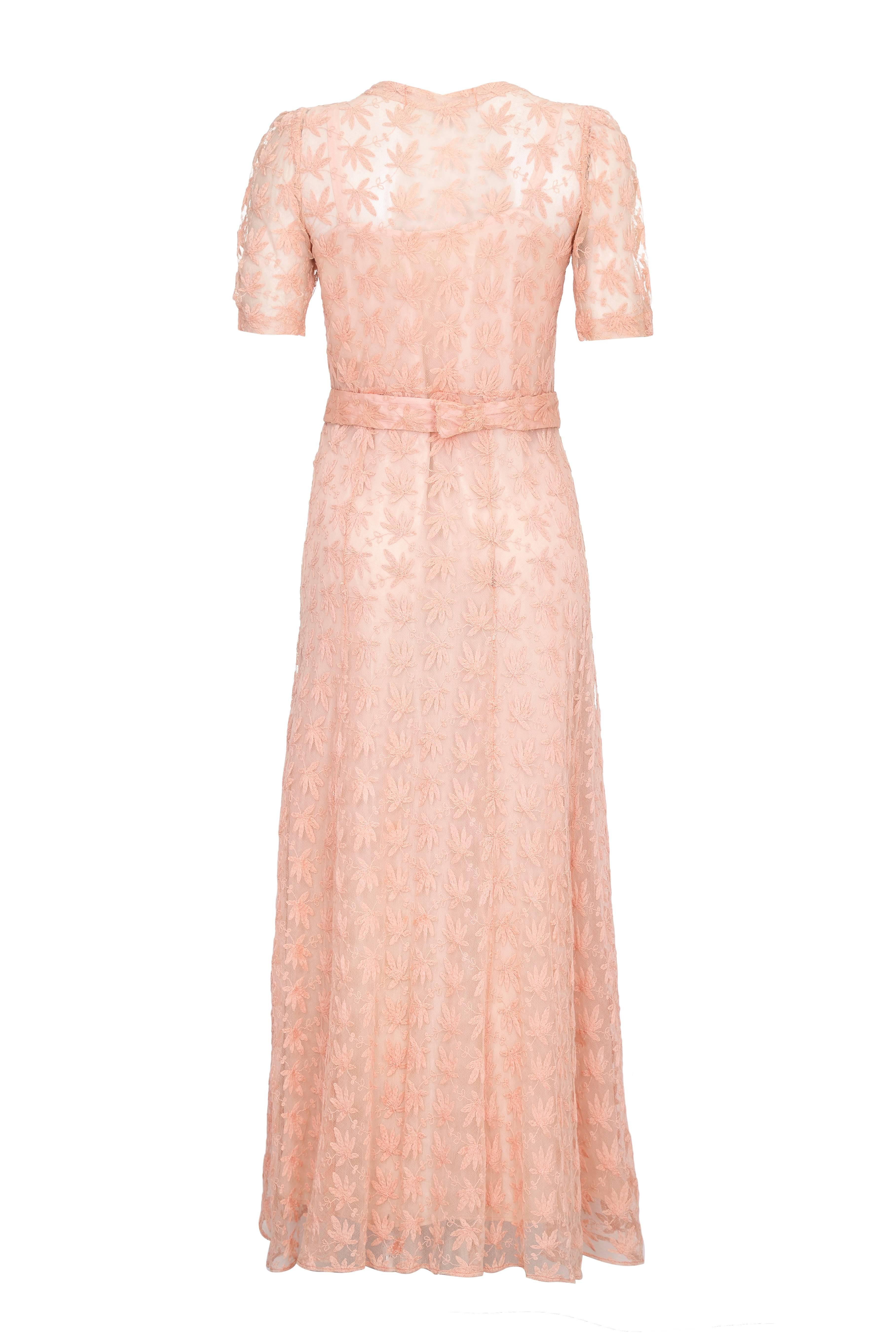 Dieses bezaubernde Vintage-Kleid aus den 1930er Jahren aus blassrosa durchscheinendem Netz mit zarter Blattstickerei wird mit einem passenden Gürtel geliefert, der auf der Rückseite mit Haken und Ösen befestigt wird. Dieses wunderschöne Kleid mit