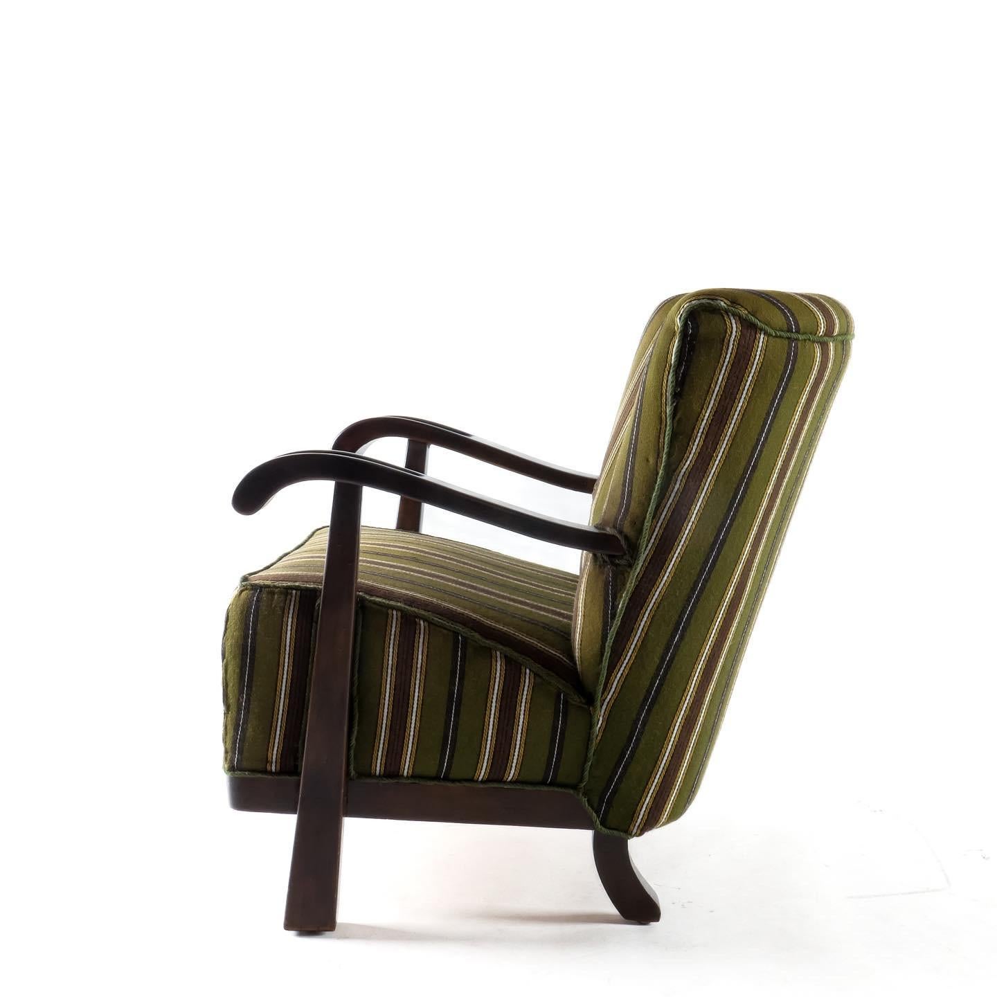 A classic silhouette armchair from Magnus Oleson circa 1930s. Dark stained Beech frame and striped wool upholstery which appears to be original. Dramatic side profile with button tufted backrest. Presents well and is comfortable although