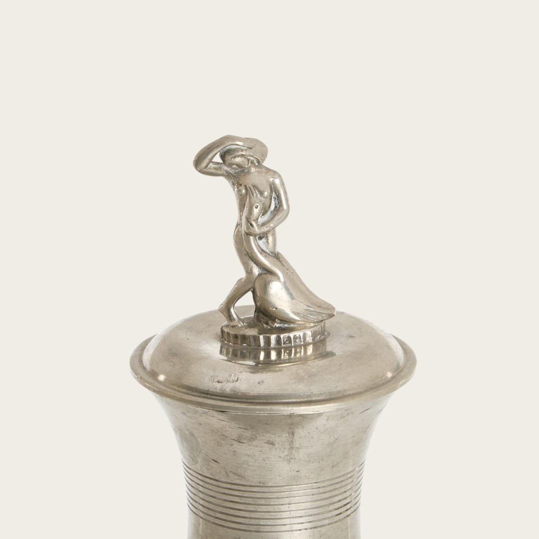 Swedish Grace vase or lidded urn with a decorative lid featuring a sculptural figure atop. A detailed figure is a woman with a swan. The vase has ribbed linear engraving throughout the mouth and the stem. Design attributed to Sylvia Stave.