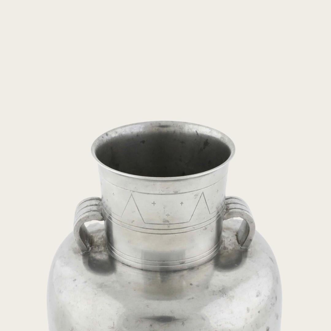 1930s, Sweden. This pewter vase features geometric and star engravings around the rim, with smooth, rounded handles on each side. The maker’s mark is located on the bottom.