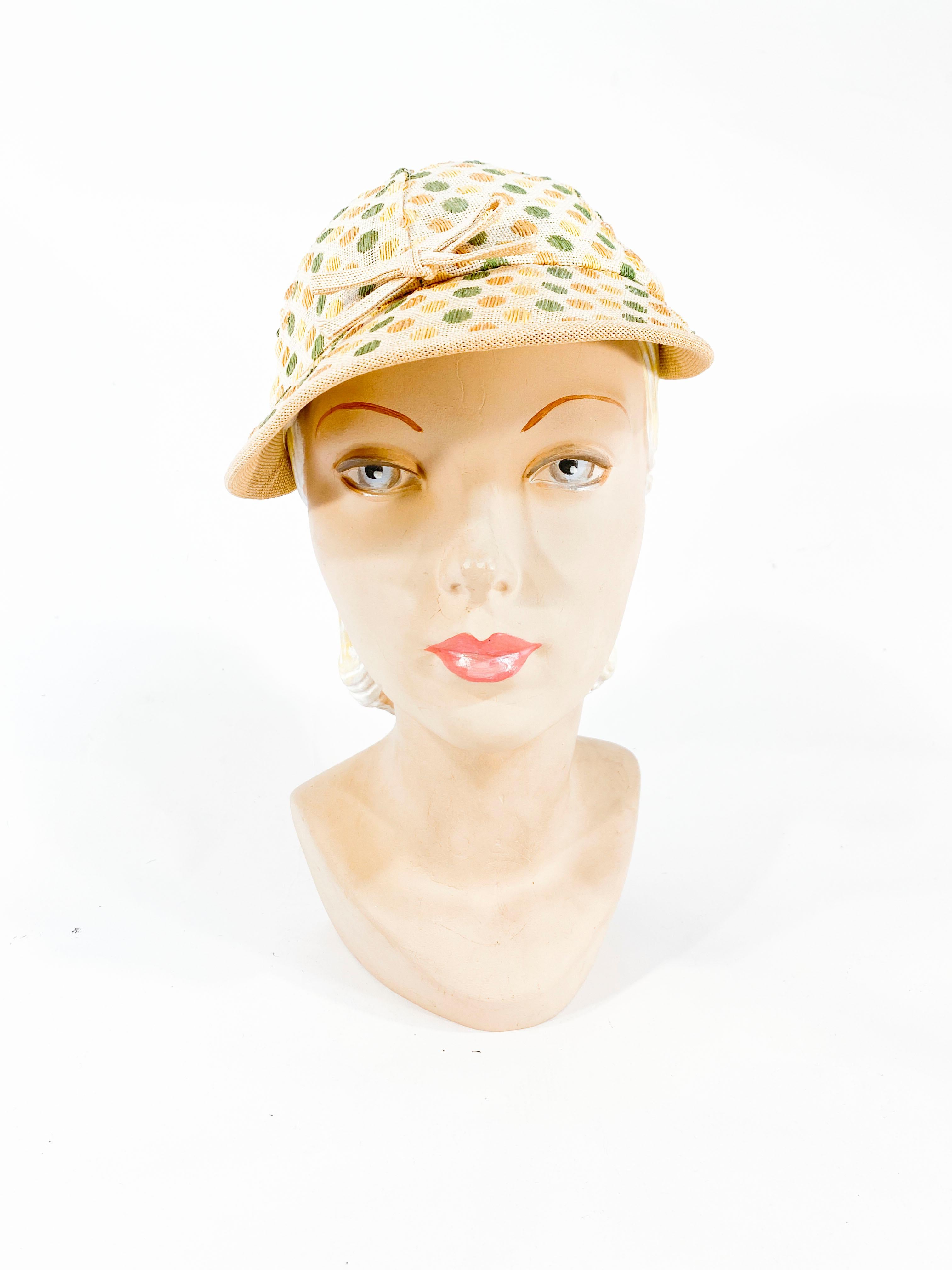 1930s polka-dot sports/golf hat featuring shades of green, gold, and yellow dots woven into a coated canvas. The hat is finished with a tied bow centered on the front brim and a covered button top. 