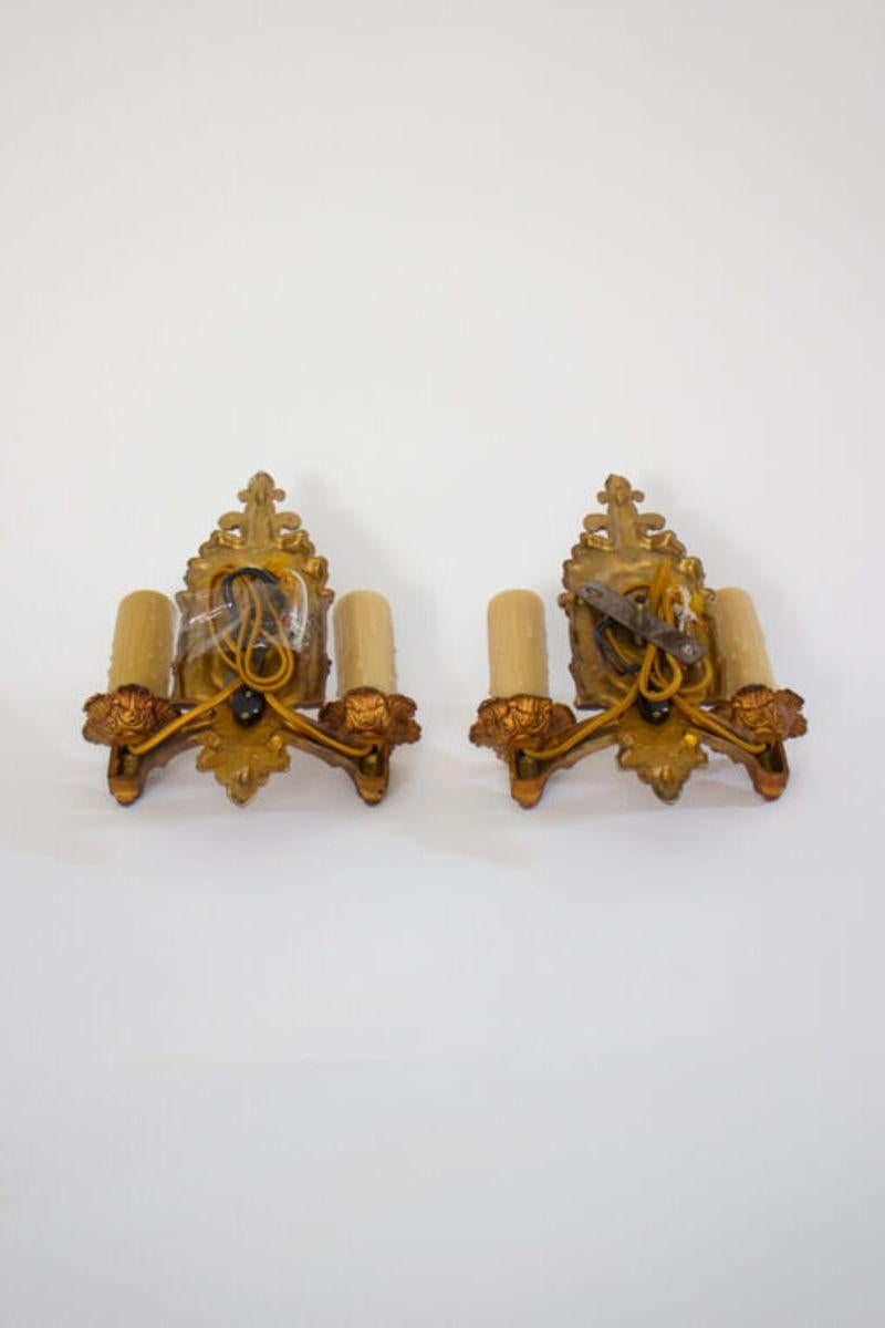 Two arm art deco renaissance revival sconces. White Metal with original polychrome painted finish. C. 1930. Gold with red and green. Switch on backplate. Design sits close to wall, can be used in smaller spaces, hallways or stairways.  Reminiscent