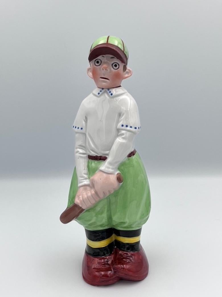 Este encantador decantador figurativo de porcelana de los años 30 es una deliciosa representación de un jugador de críquet, que encarna el espíritu lúdico de la época. El decantador está meticulosamente elaborado, con un diseño detallado en el que