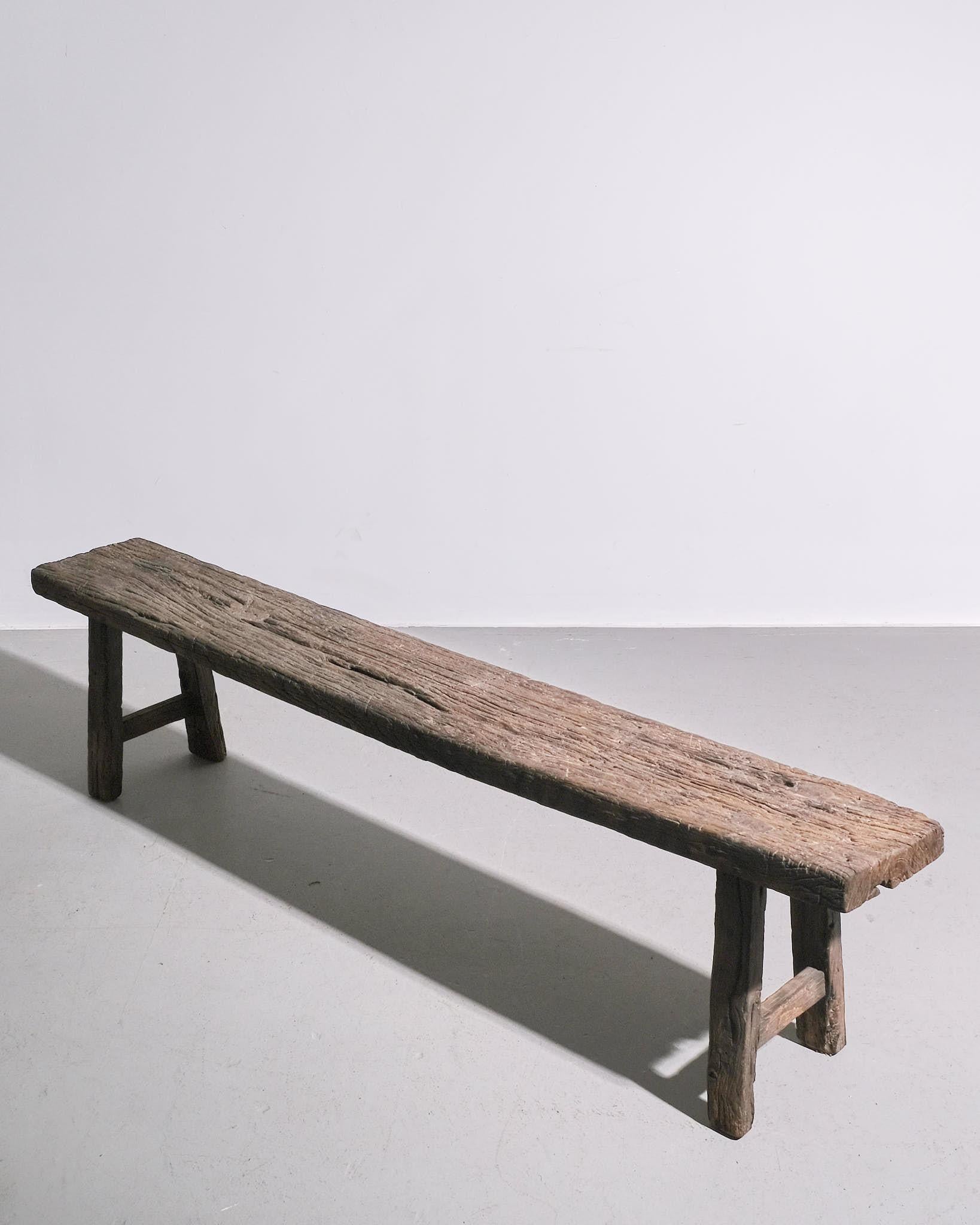 A robust and utilitarian Belgian bench from the 1930s, crafted from solid wood. The design is simple and unembellished, with a flat plank seat supported by sturdy legs, showcasing traditional joinery techniques. Aged patina and visible wear reflect