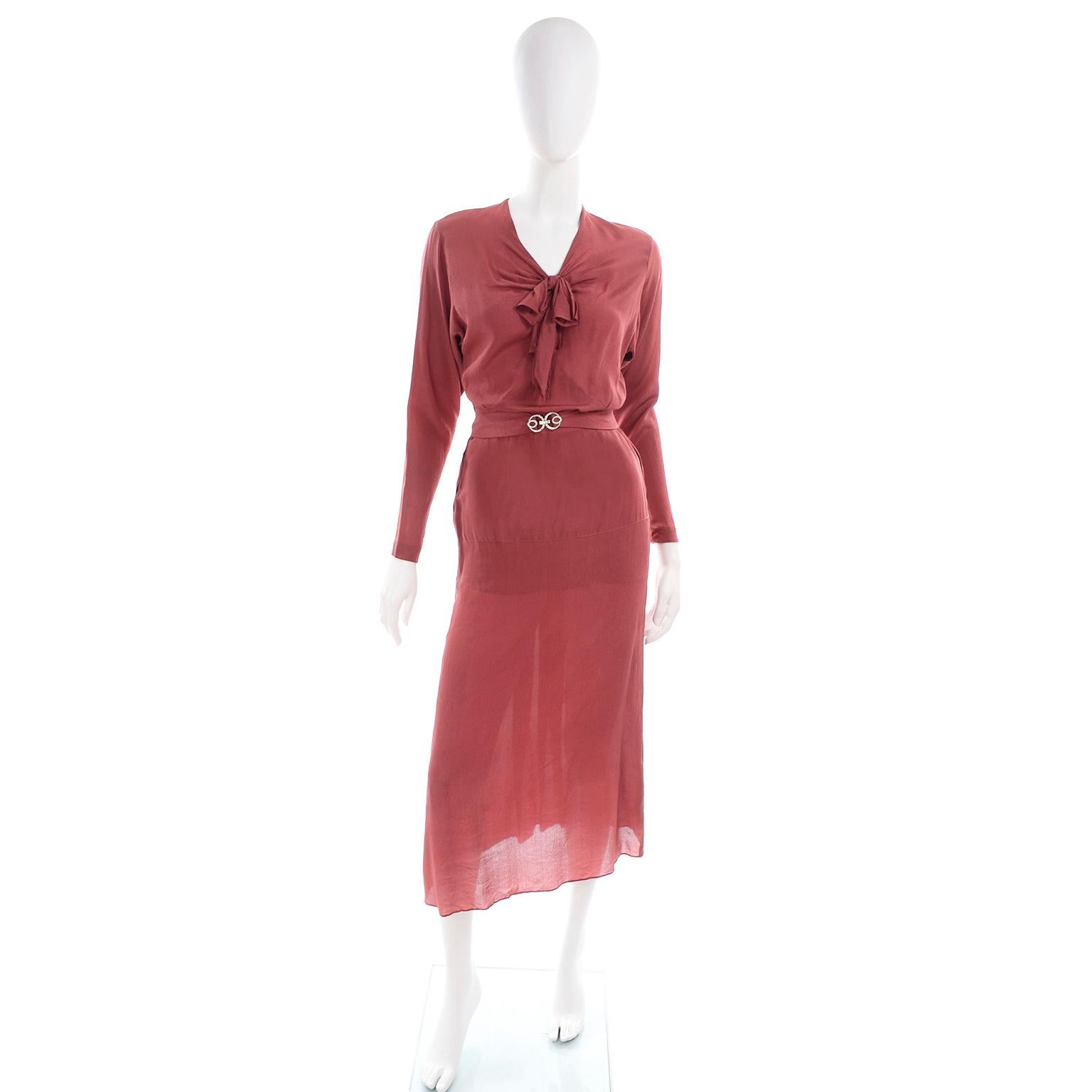 This is a vintage 1930's two piece rust red silk dress with a matching belt with original sash buckle. This top of the dress has long sleeves with gathered tucks on the elbows, a V neckline and a bow. The skirt has back pleats and hits a few inches