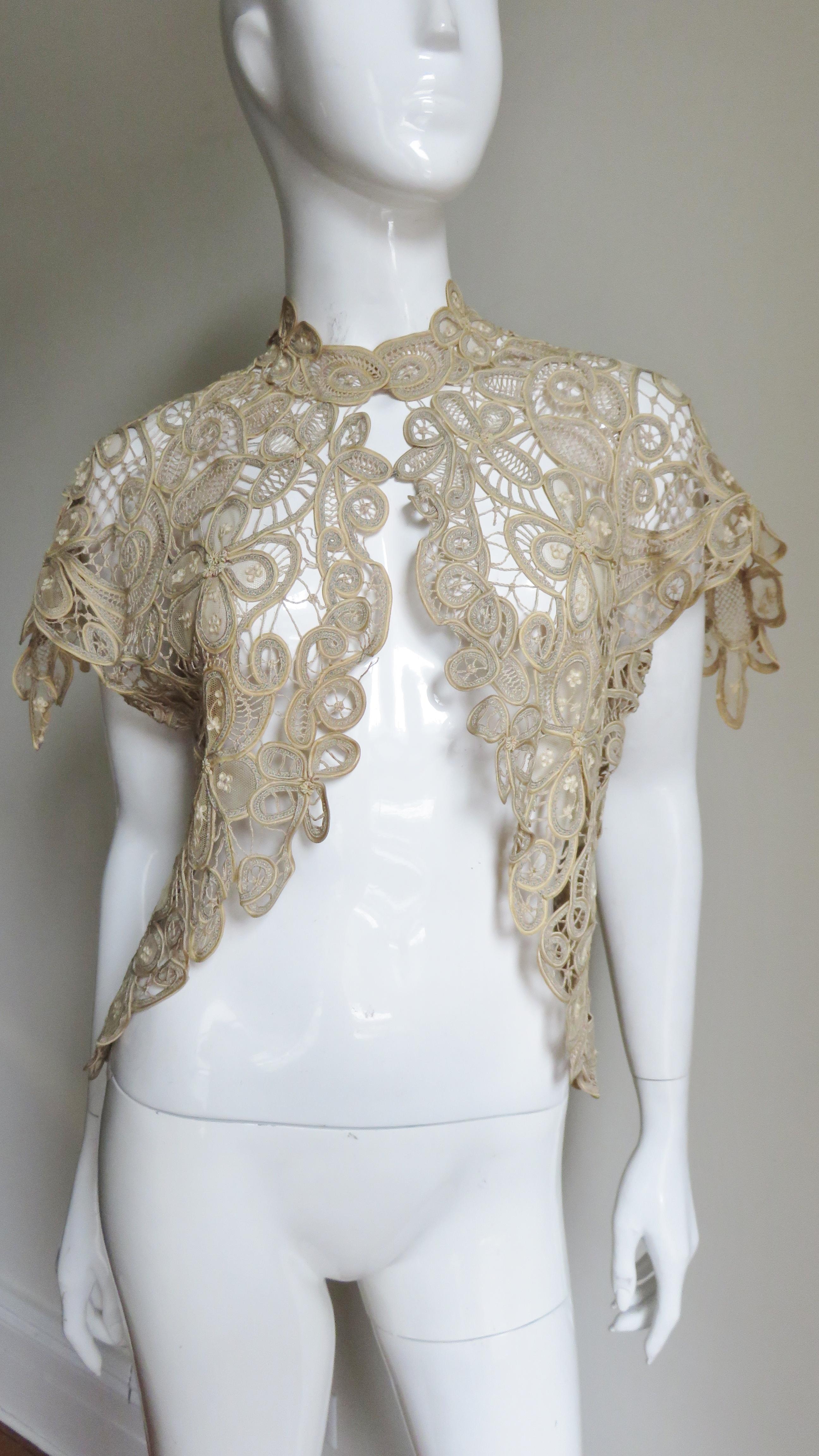 An intricate, stunning, vintage beige silk lace jacket, bolero, shrug, vest in varying stitches and patterns of flowers and petals- very elaborate. The shoulders are extended forming cap sleeves.  The hem which dips longer at the sides, sleeves, and