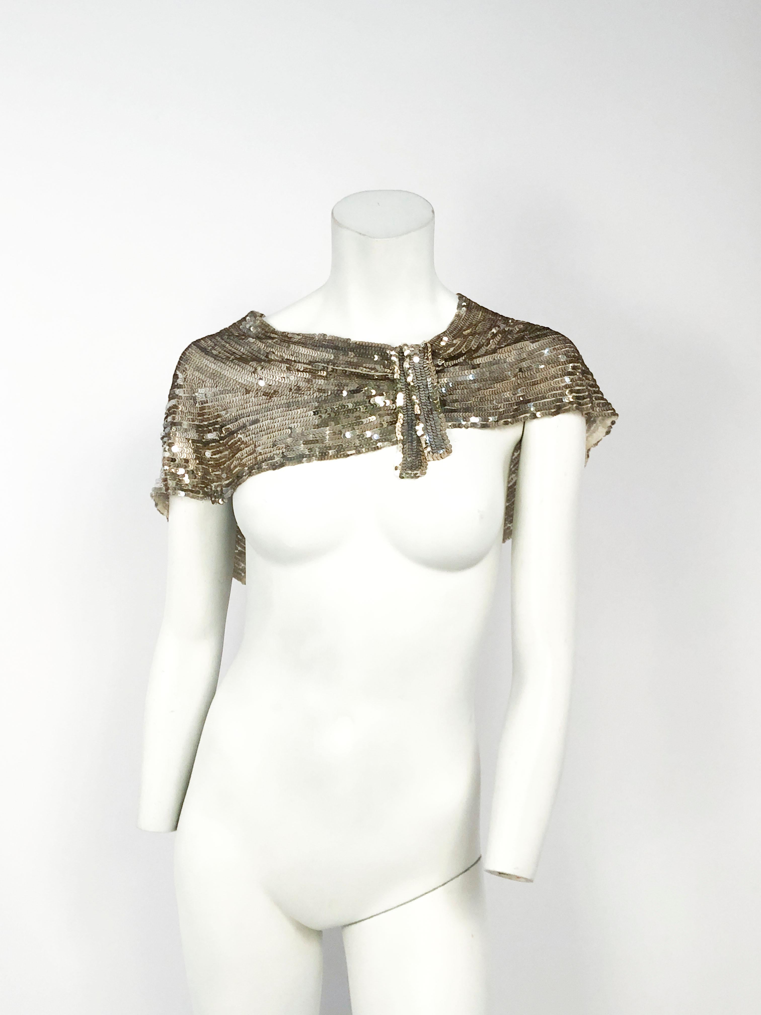 1930s capelet entirely covered with silver sequin closed with an off-centered flounce accented with a faint gold border sequin.  The draped structure of this piece complements the brilliant silver sequin. Based on the shoulder measurement, this