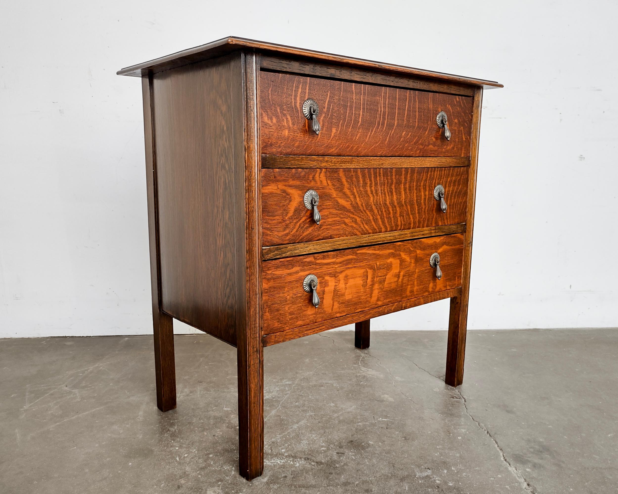 1930s tiger oak chest of three drawers. Six original solid brass teardrop pulls with a lovely patina. Beautiful wood grain showcased over the entire piece. Classic simple design distinctive of American early 20th century. Overall excellent