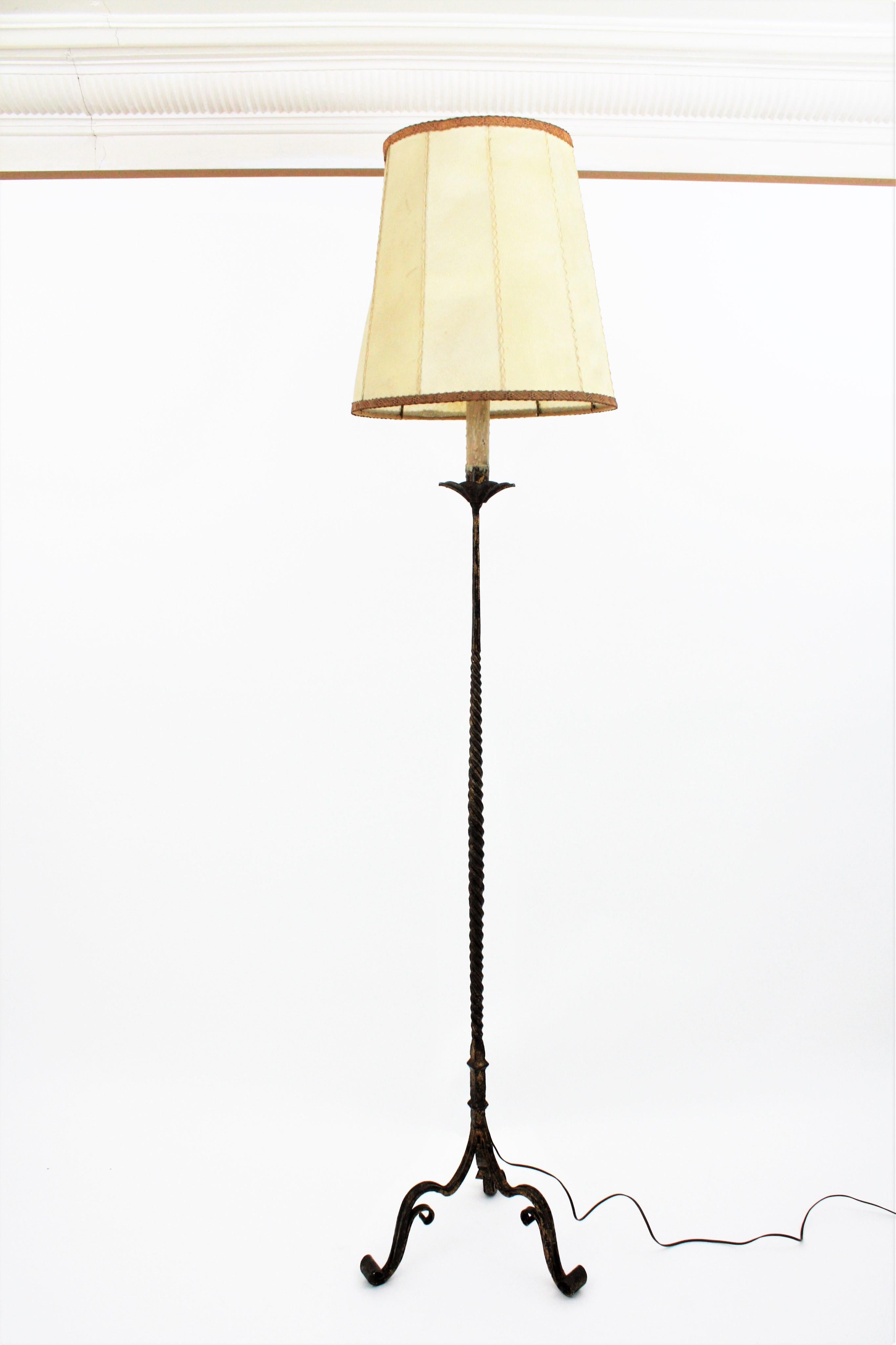 Hand-hammered gilt iron standing lamp with twisted stem with original vellum shade raised on a tripod base, Spain, 1930s-1940s.
Stylish Gothic accents, nice distressed aged patina retaining rests of gold leaf gilt finish.
On sale with its antique
