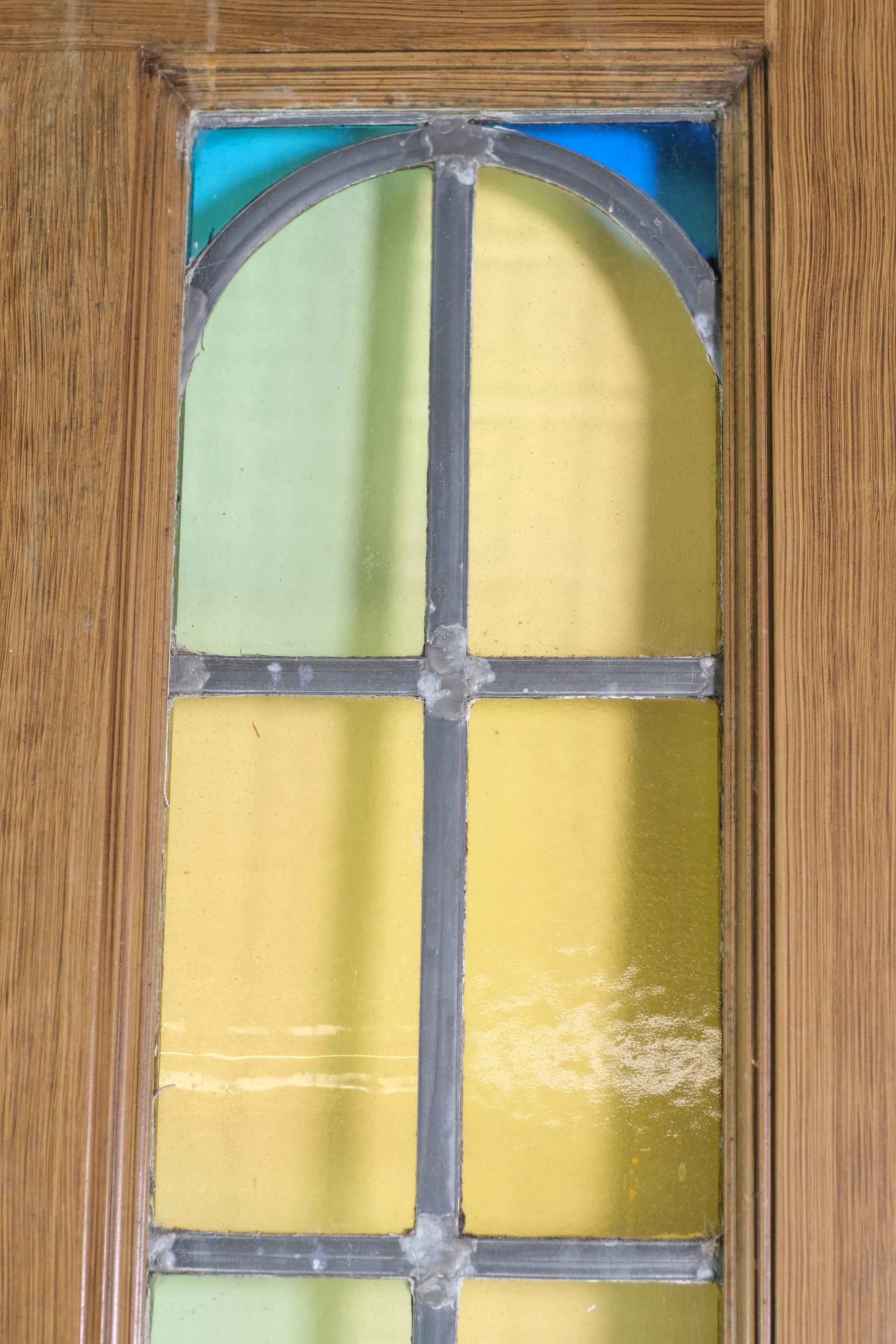 These 1930s steel doors have a faux oak finish and leaded stained glass arched windows.  The leaded windows are in good condition and have vibrant colors including yellow, green and blue.  The bottom of each door includes two recessed vertical