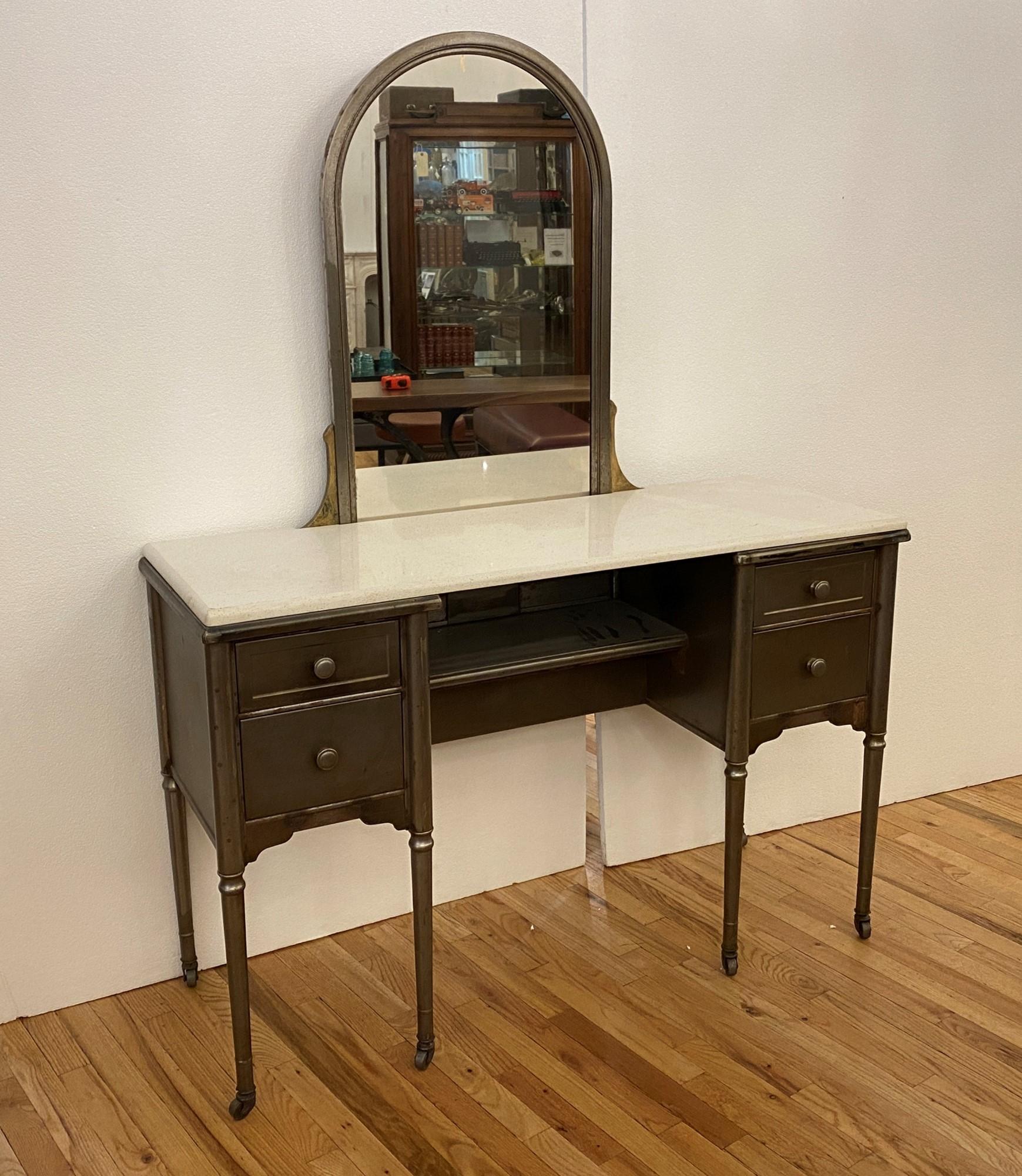 This is a 1930s steel metal vanity with mirror. It originally was produced with a faux finish, which has been stripped, and the vanity then sealed with a lacquer finish. There are four drawers and a lower middle shelf, which style was popular in the