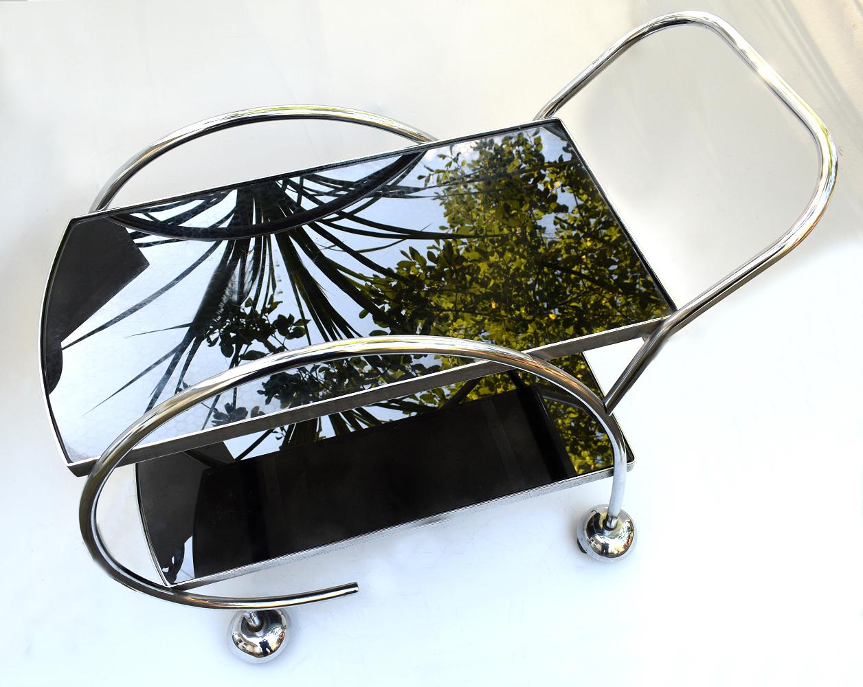 Stylish English 1930s Art Deco two-tier chrome and black glass drinks hostess trolley bar cart. This design is a little more unusual in shape than you normally find and is a lot more substantial in weight, quality and is very sturdy. If glam is your