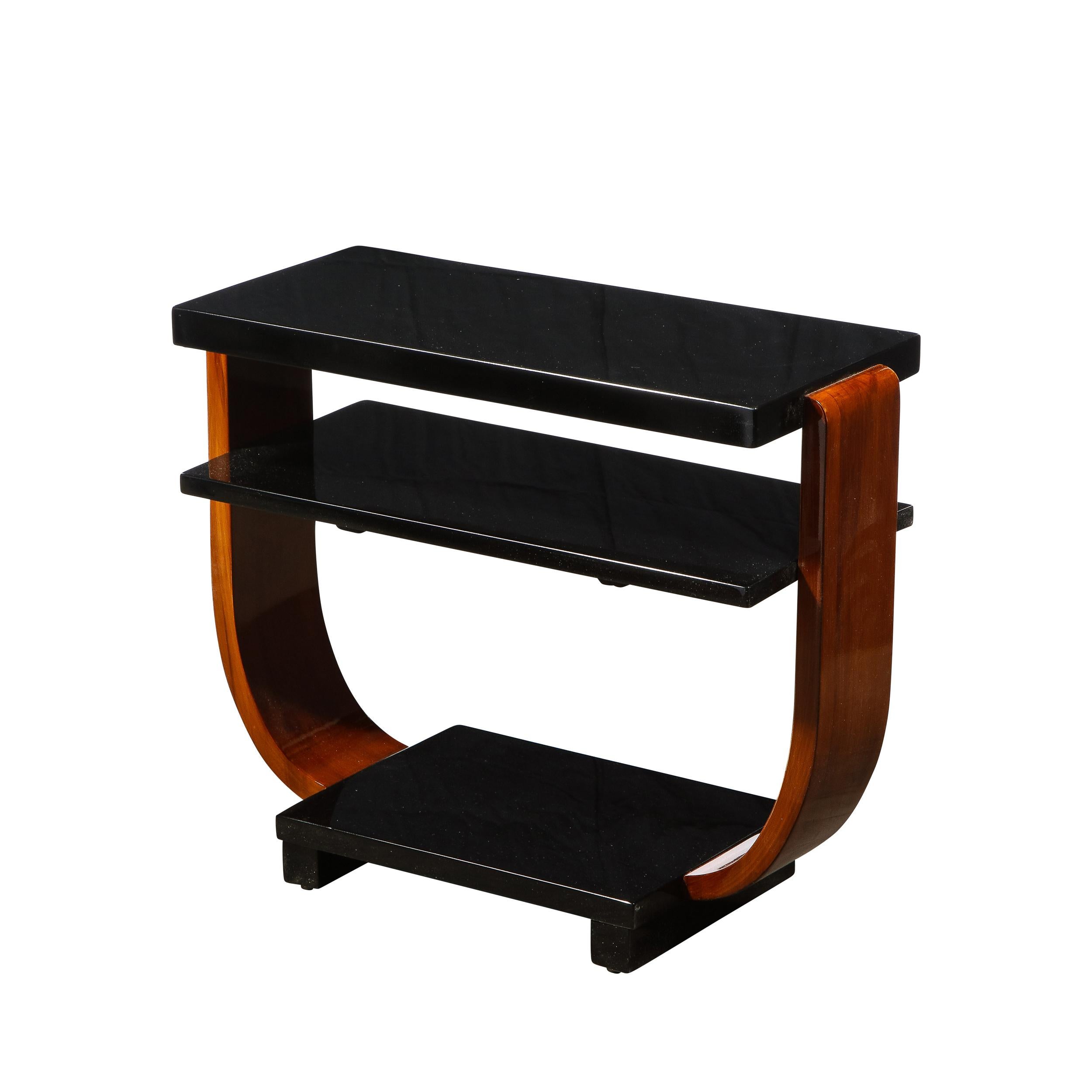 These elegant Art Deco Machine Age side tables was realized in the United States circa 1935. They feature curvilinear walnut legs connected to a black lacquer base which supports the lustrous black lacquer two tier top. With their clean modernist