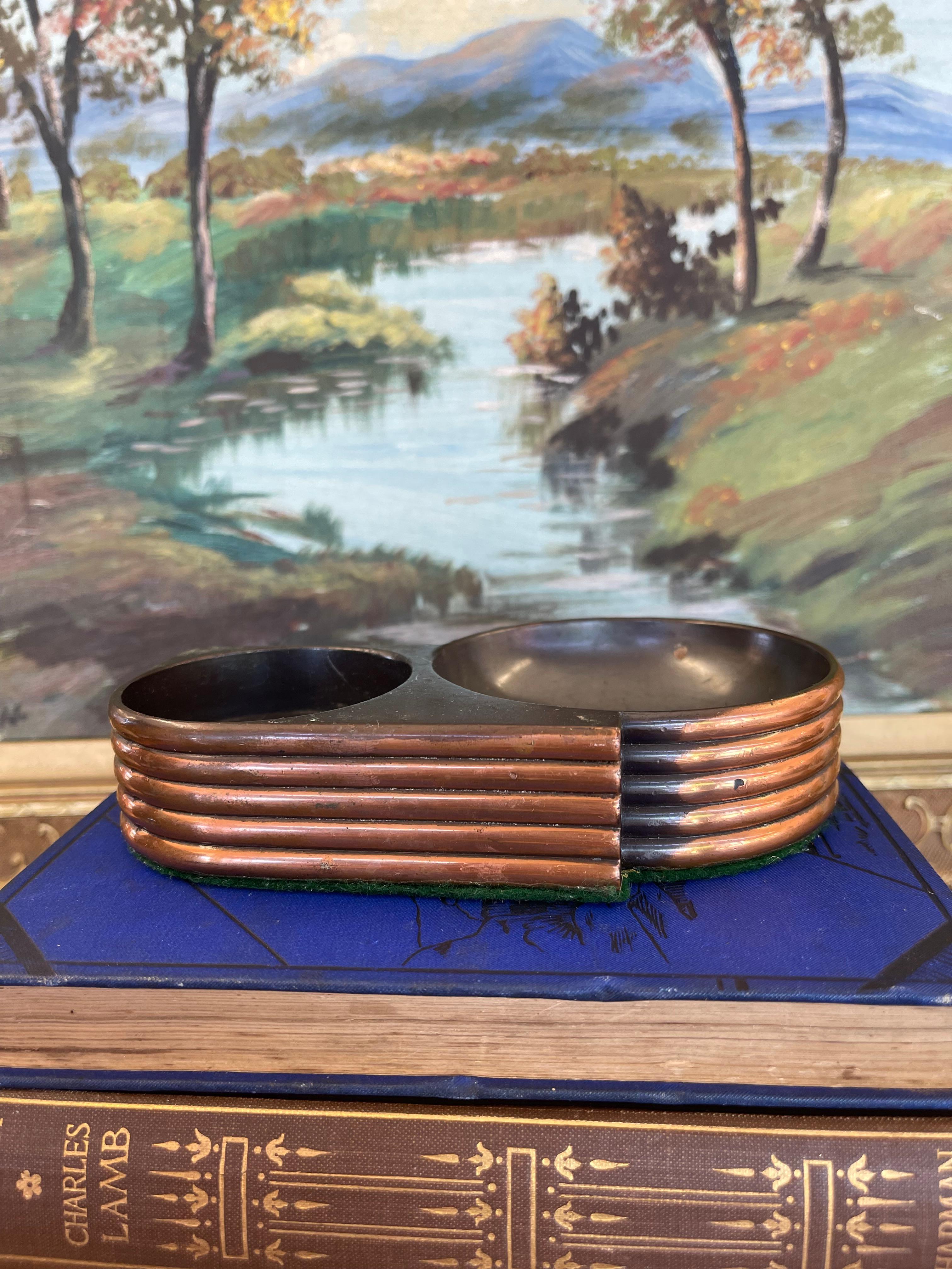 An 1930s style Art Deco ashtray featuring a sleek Machine Age aesthetic. Constructed from deep brown possible Bakelite and accented with polished copper toned ribbed bands along the sides, this compact piece embodies the streamlined elegance of the
