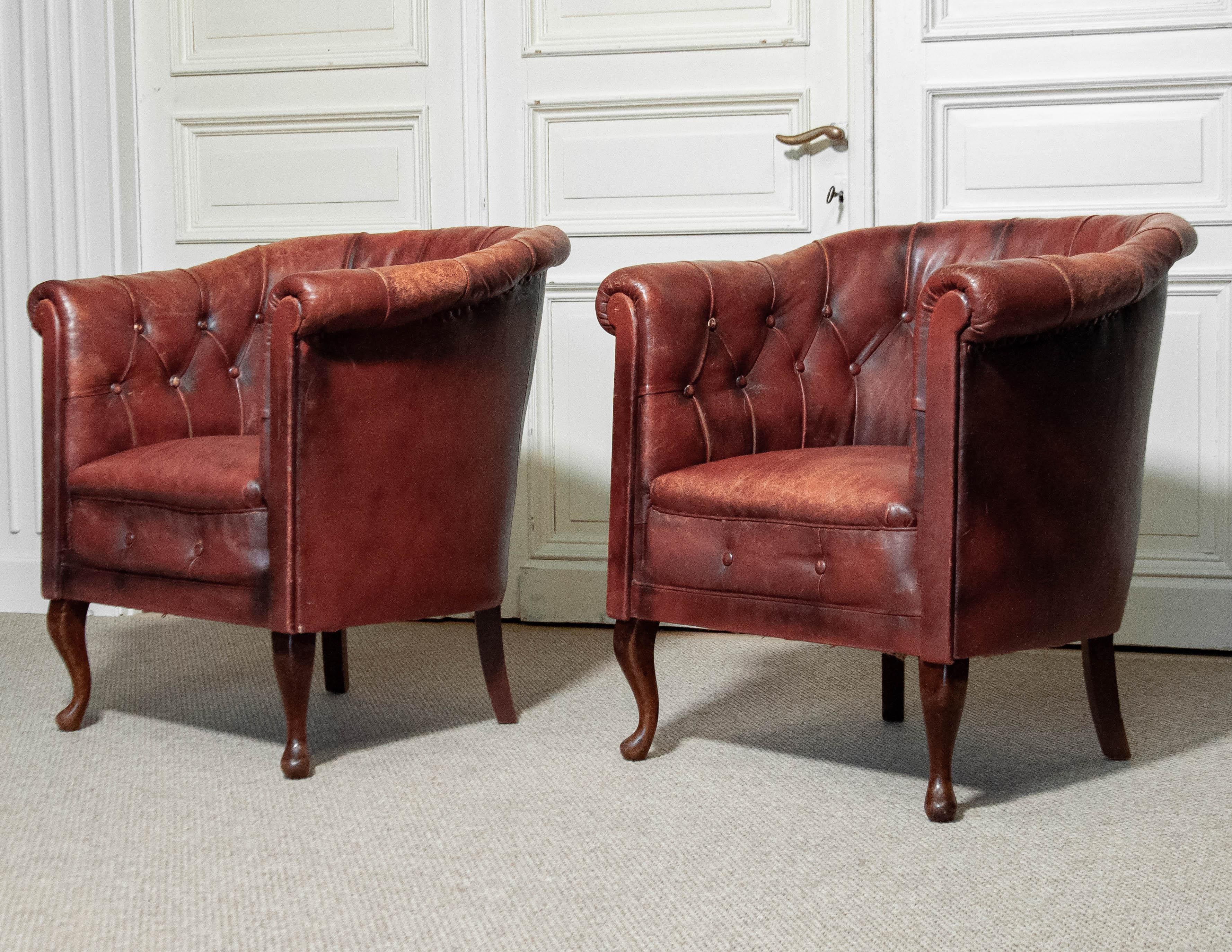 A beautiful pair of early 1900s Swedish Chesterfield club chairs, featuring deep button-tufted leather upholstery with a rich, aged patina. The chairs have been fitted with new webbing for enhanced durability, while the worn armrests add to their