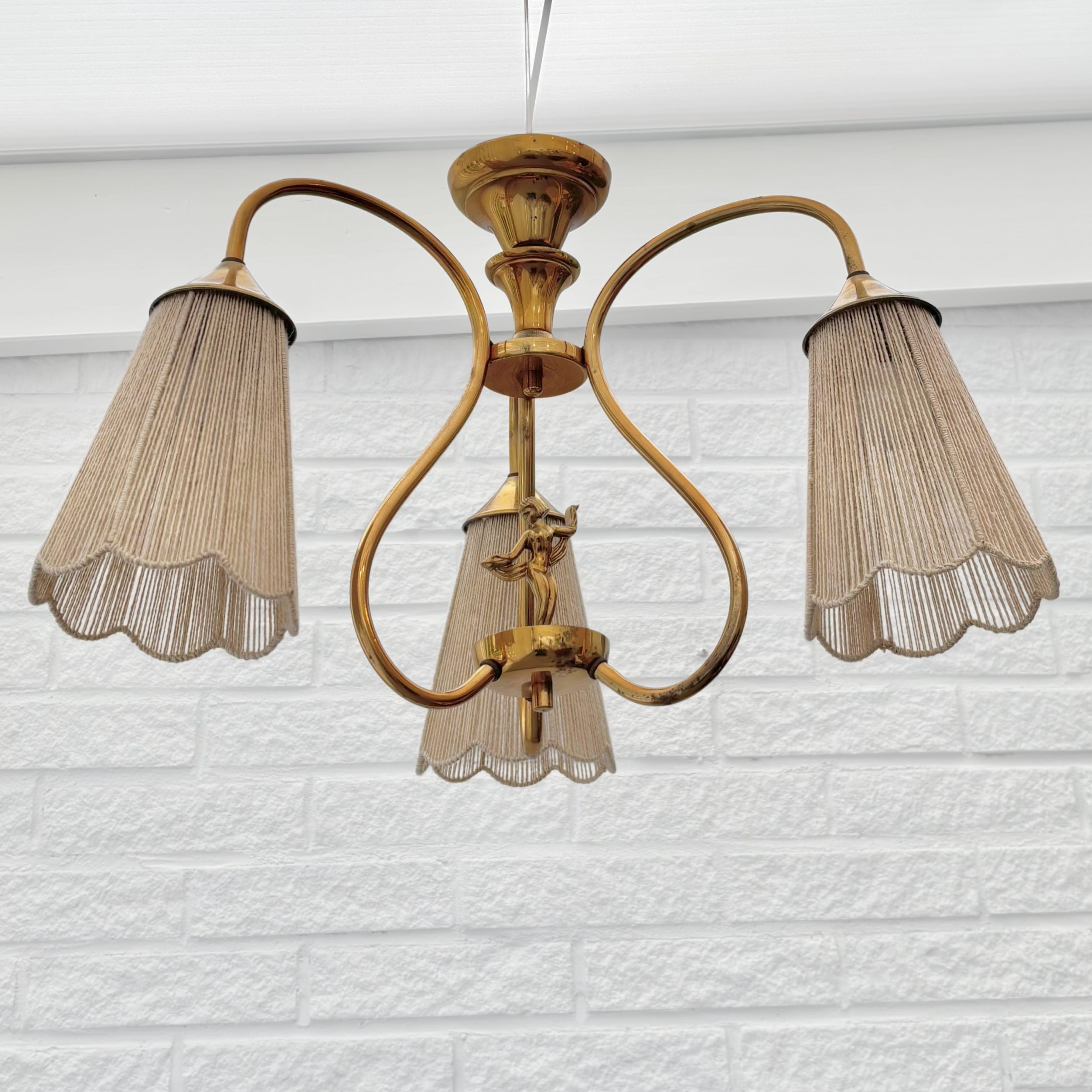 Preciosa lámpara colgante art decó sueca atribuida al fabricante Ystad Metall. Fabricado en latón con una hermosa figura femenina en el centro. Tres brazos curvados que sostienen tres pantallas de lámpara trenzadas con cordón de fibra natural. Se